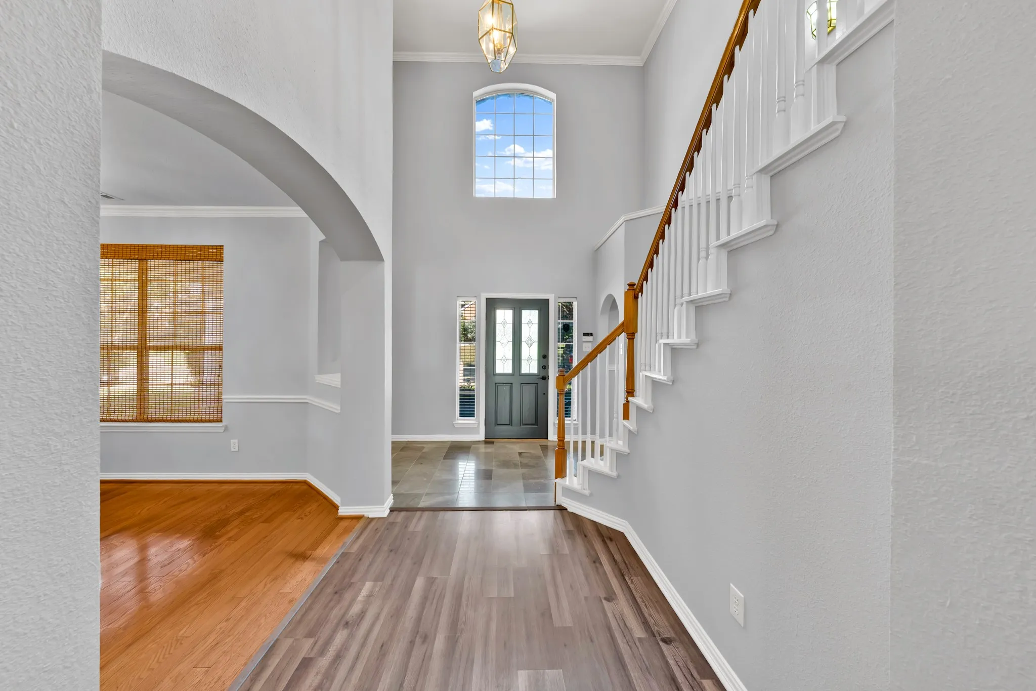 Two-story foyer with a grand staircase featuring a wood handrail, an arched doorway, and a prominent arched window