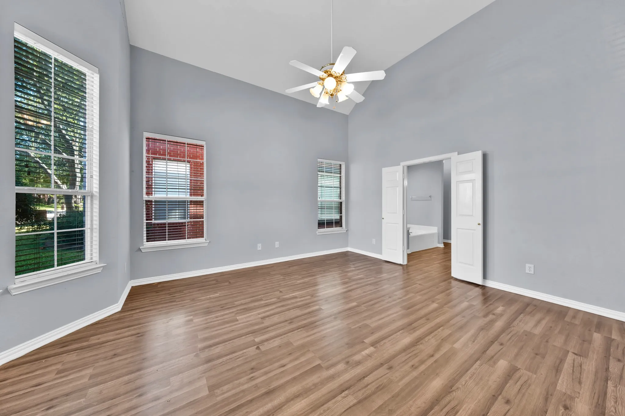 Wood-finish flooring, vaulted ceiling, ceiling fan, multiple windows, and double doors