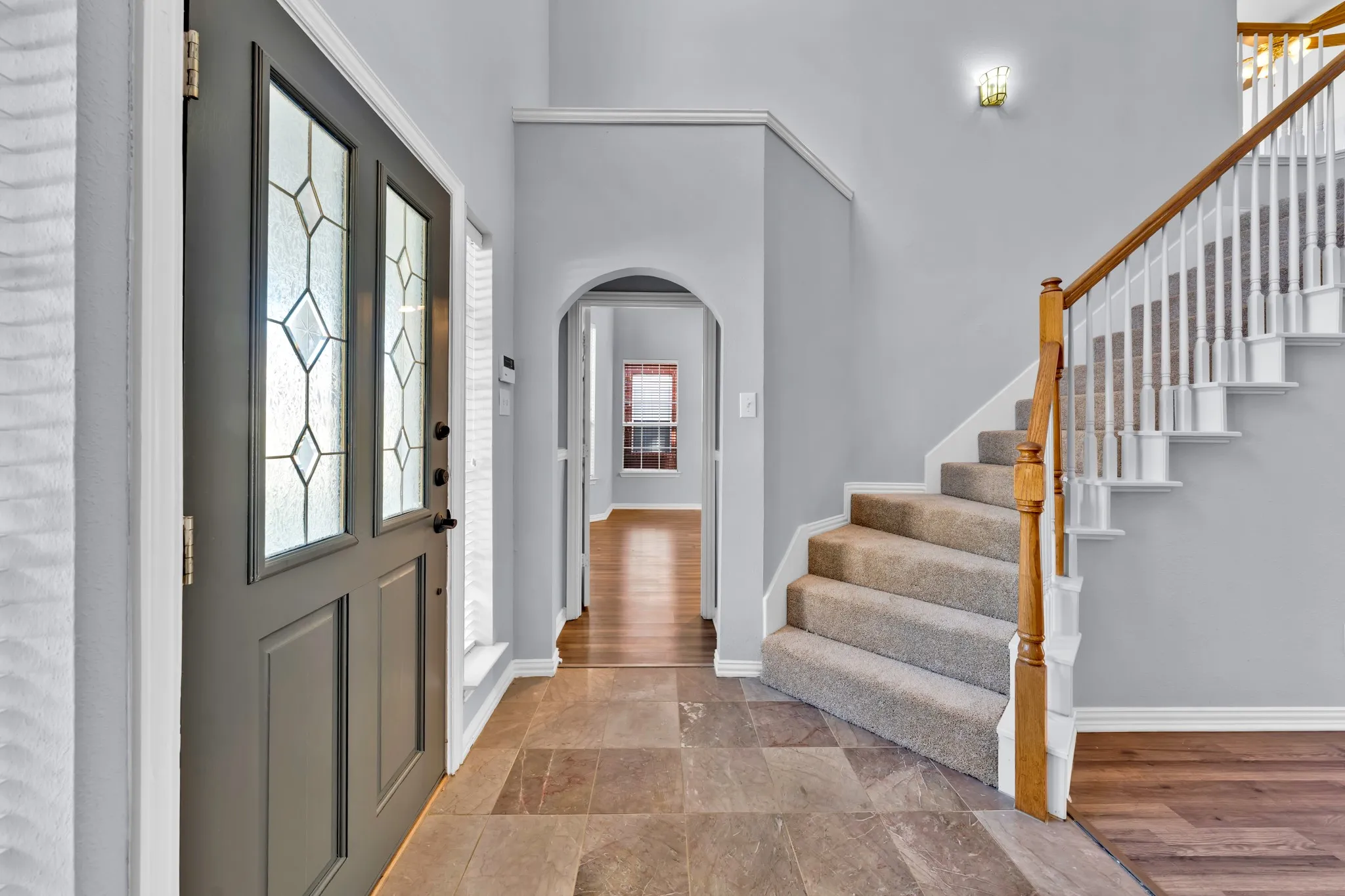 Entryway featuring a decorative glass front door, large format tile flooring, staircase with carpeted treads and wood handrails, and an arched hallway opening