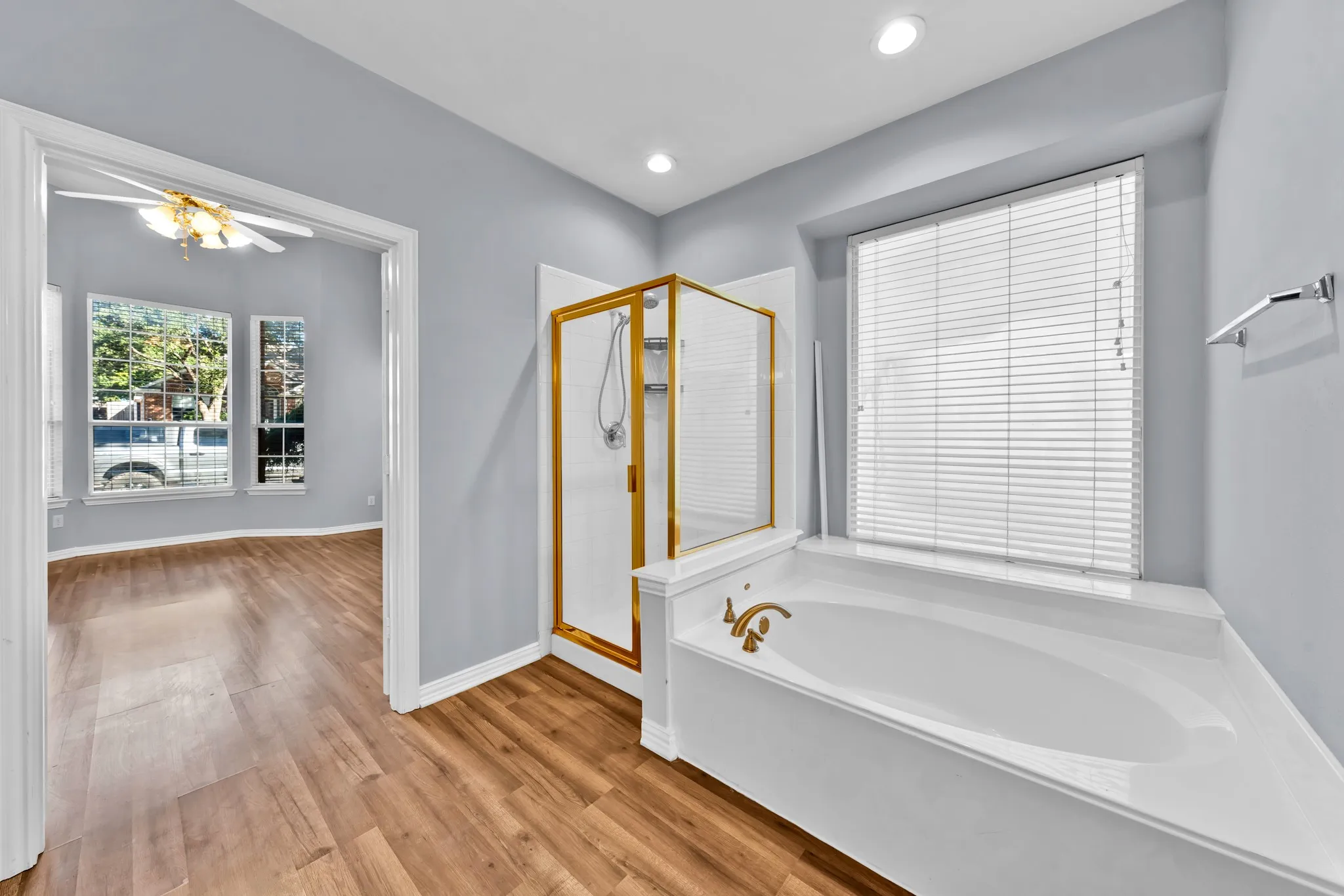 Soaking tub with a shower enclosure, recessed lighting, and wood-finish flooring
