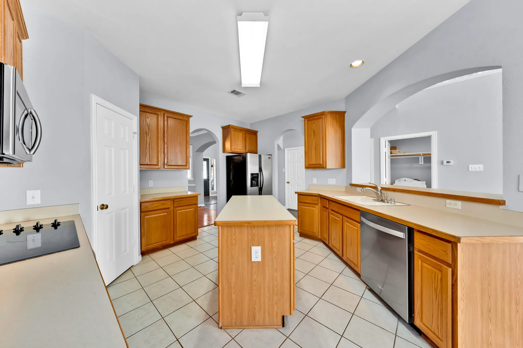 Kitchen featuring a central island, wood-finish cabinetry, tile flooring, stainless steel dishwasher, and arched wall openings