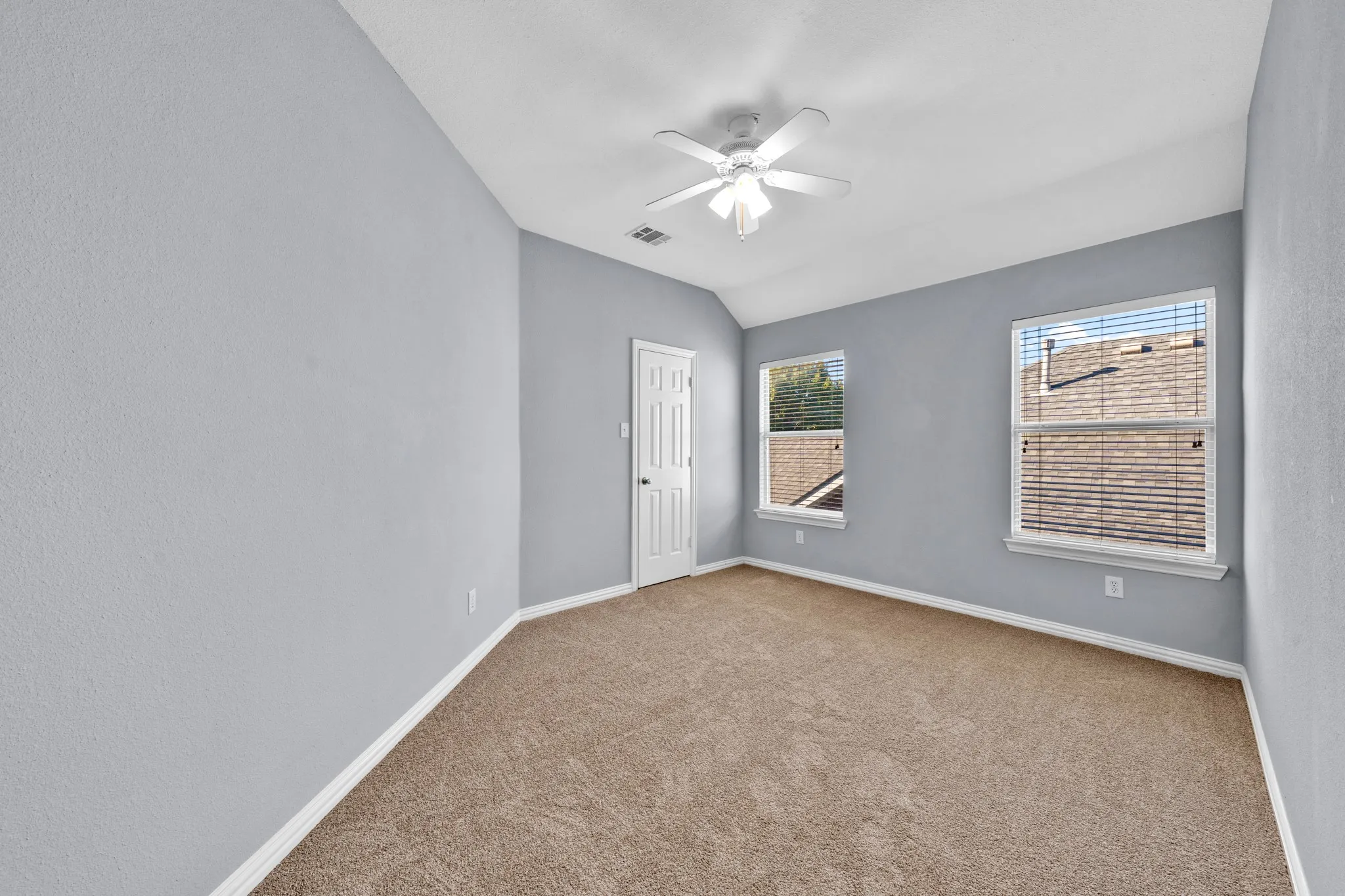 Vaulted ceiling with a ceiling fan, two windows with blinds, light blue walls, and carpet flooring