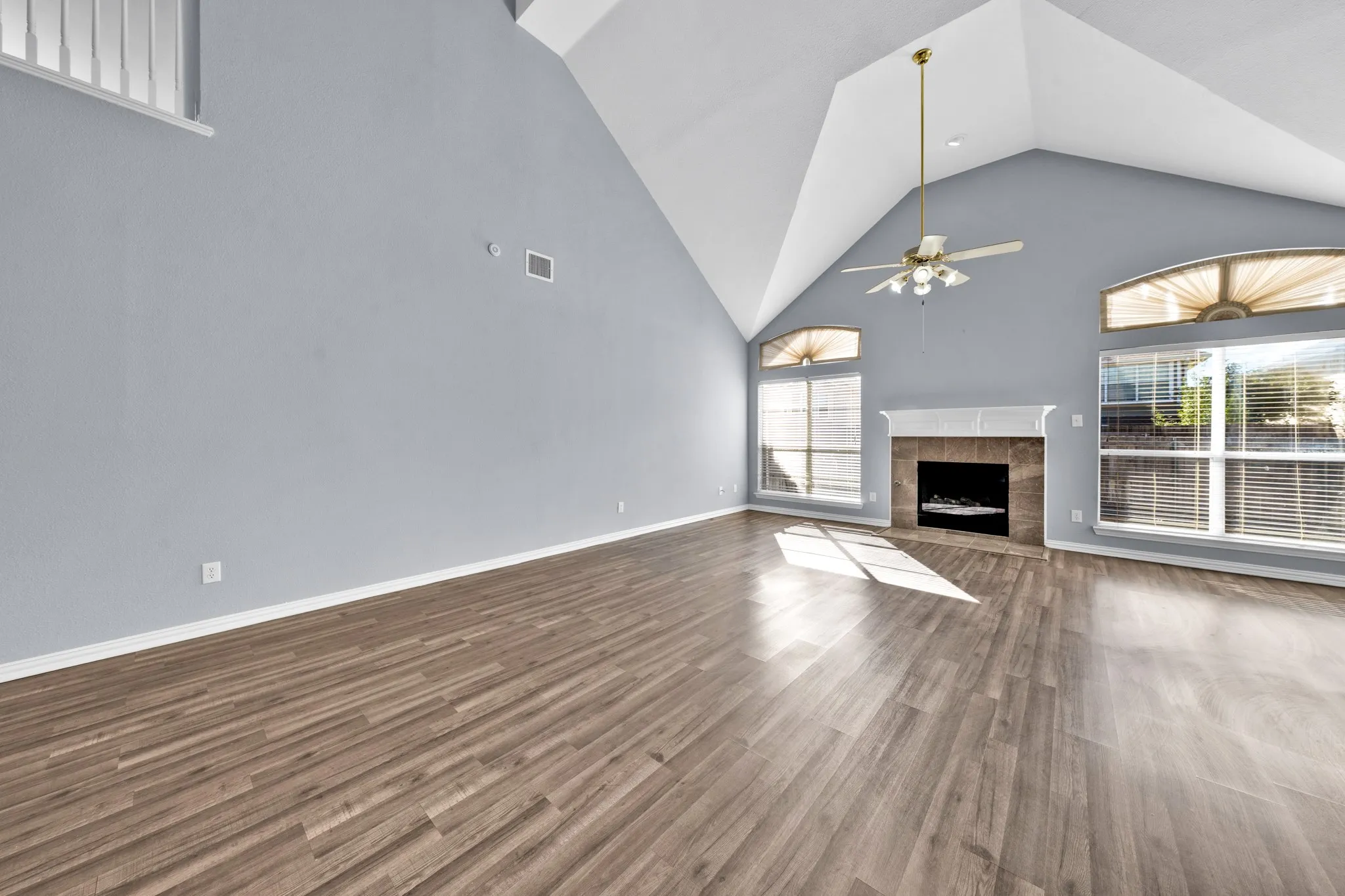 Spacious living area featuring wood-finish flooring, vaulted ceilings, a fireplace with a tile surround, a classic mantel, and multiple arched windows