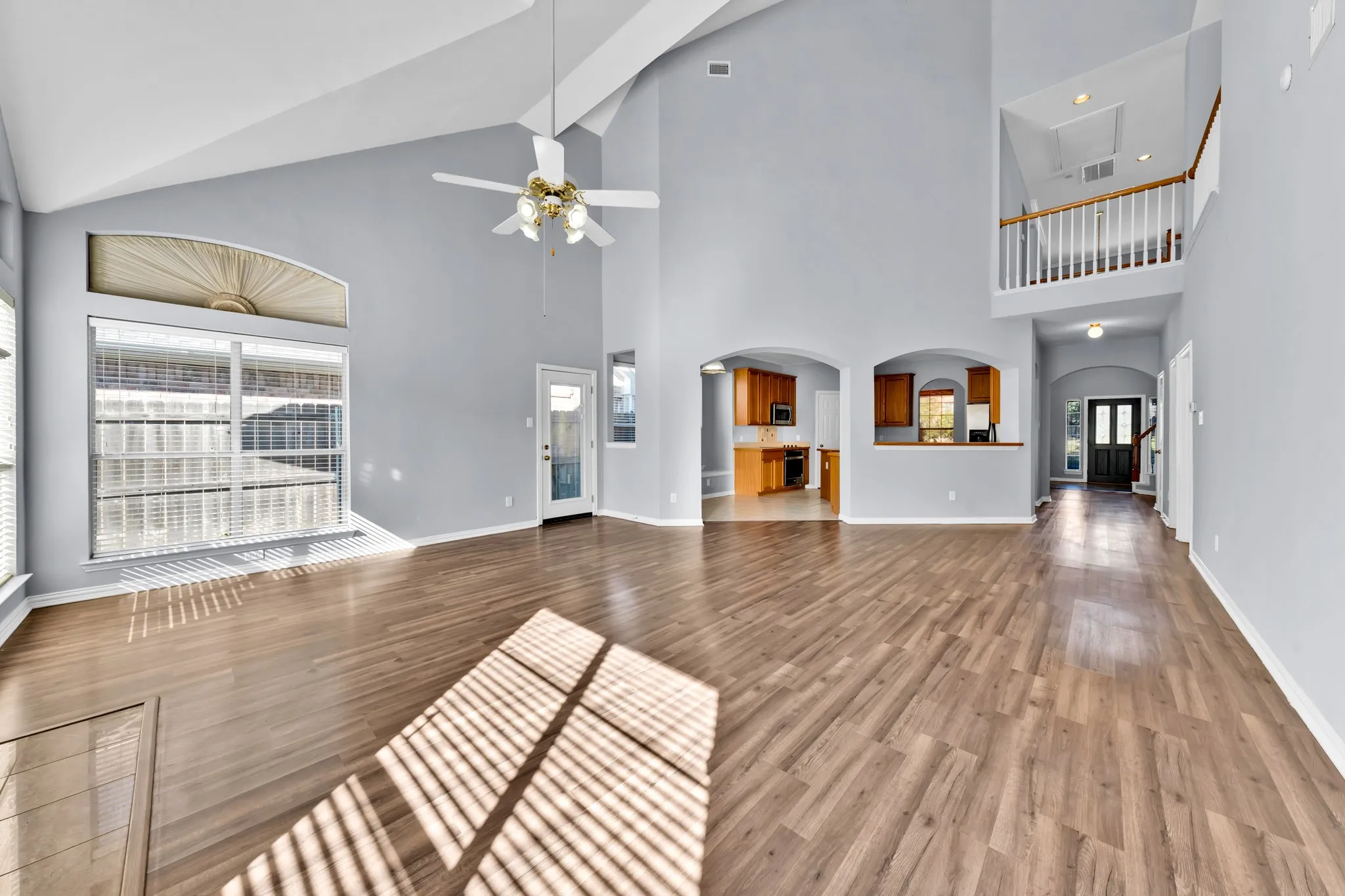 Vaulted ceiling with a ceiling fan, wood-finish flooring, arched doorways, interior balcony, and a paneled front door