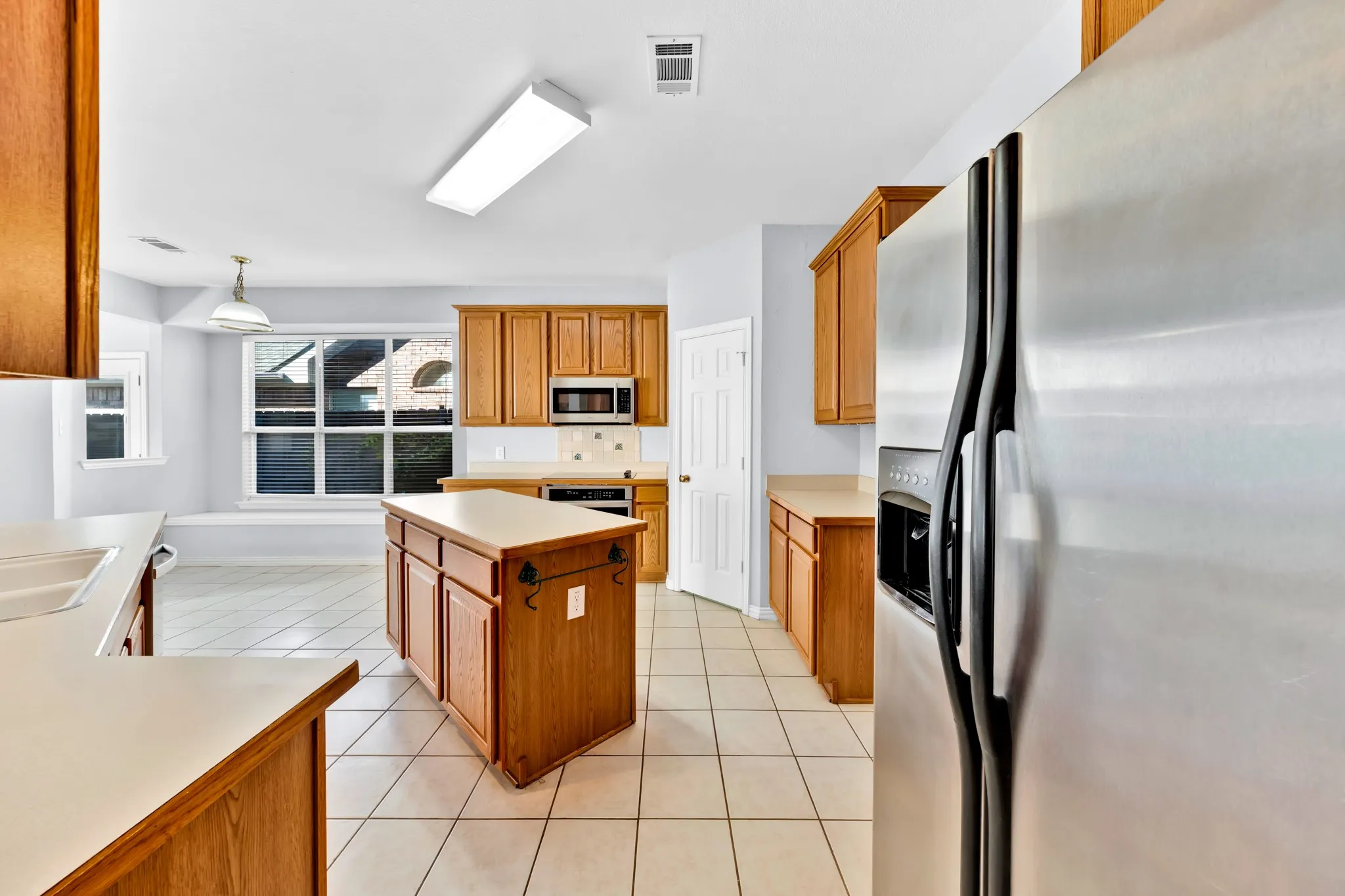 Kitchen featuring wood cabinetry, white tile flooring, stainless steel appliances, a central island, and a built-in window bench