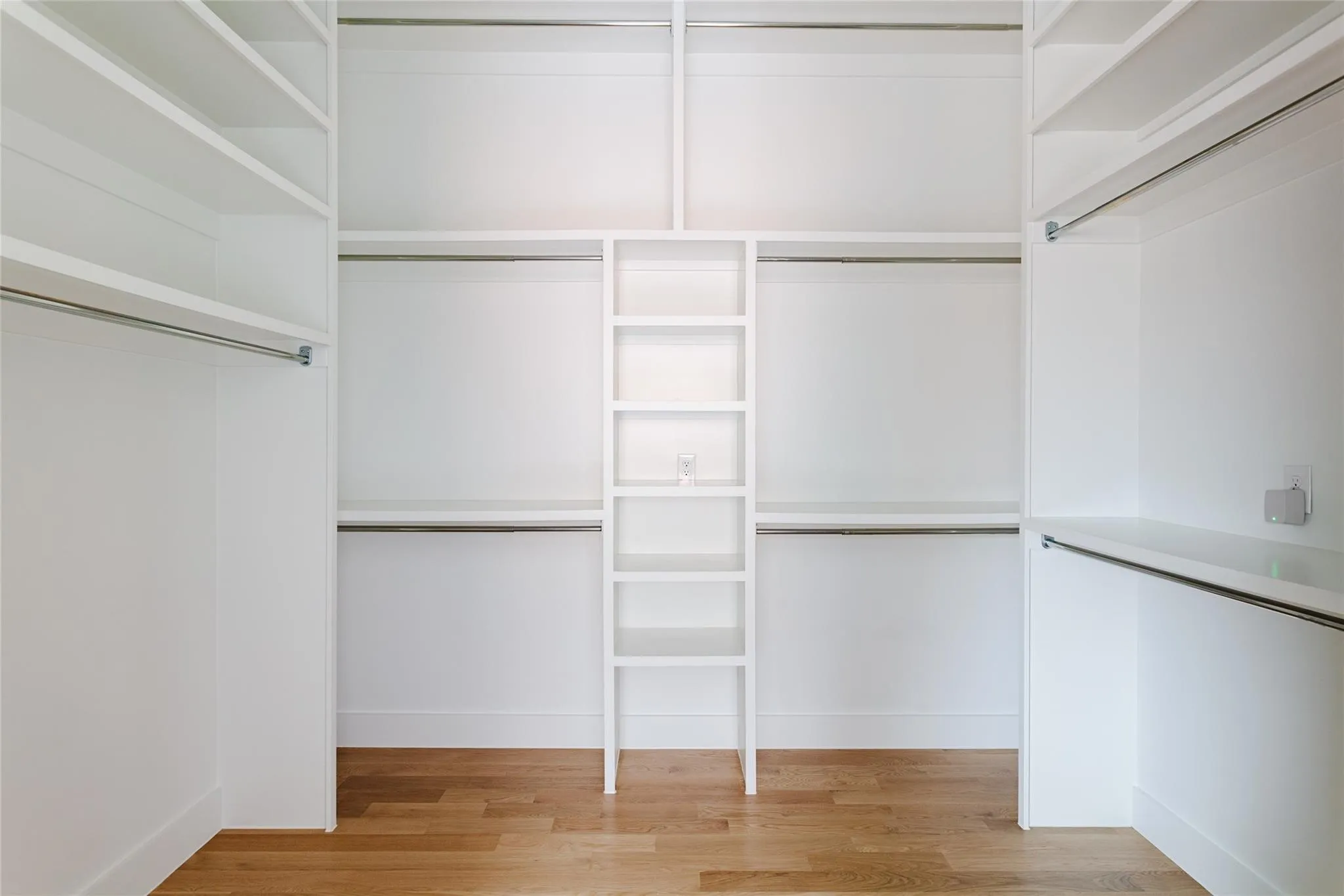 Built-in white shelving system with multiple hanging rods, integrated shelving units, and wood-finish flooring