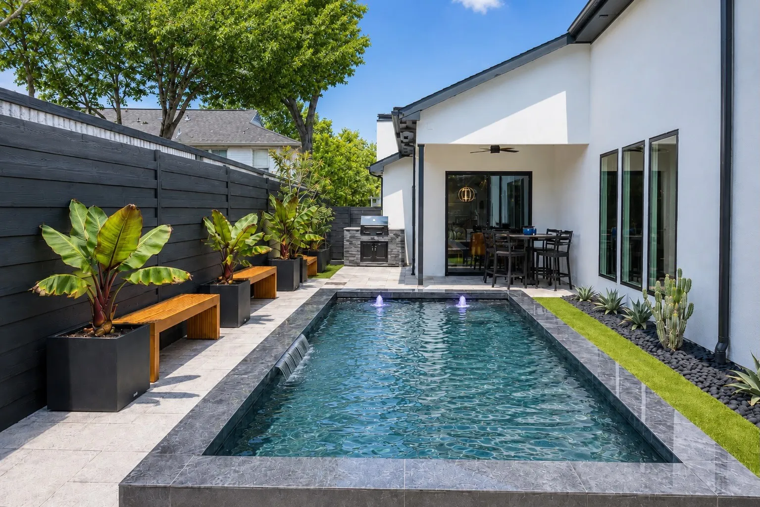 Outdoor living space featuring a rectangular pool with water features, a built-in outdoor kitchen, a covered patio, and a dark wood fence