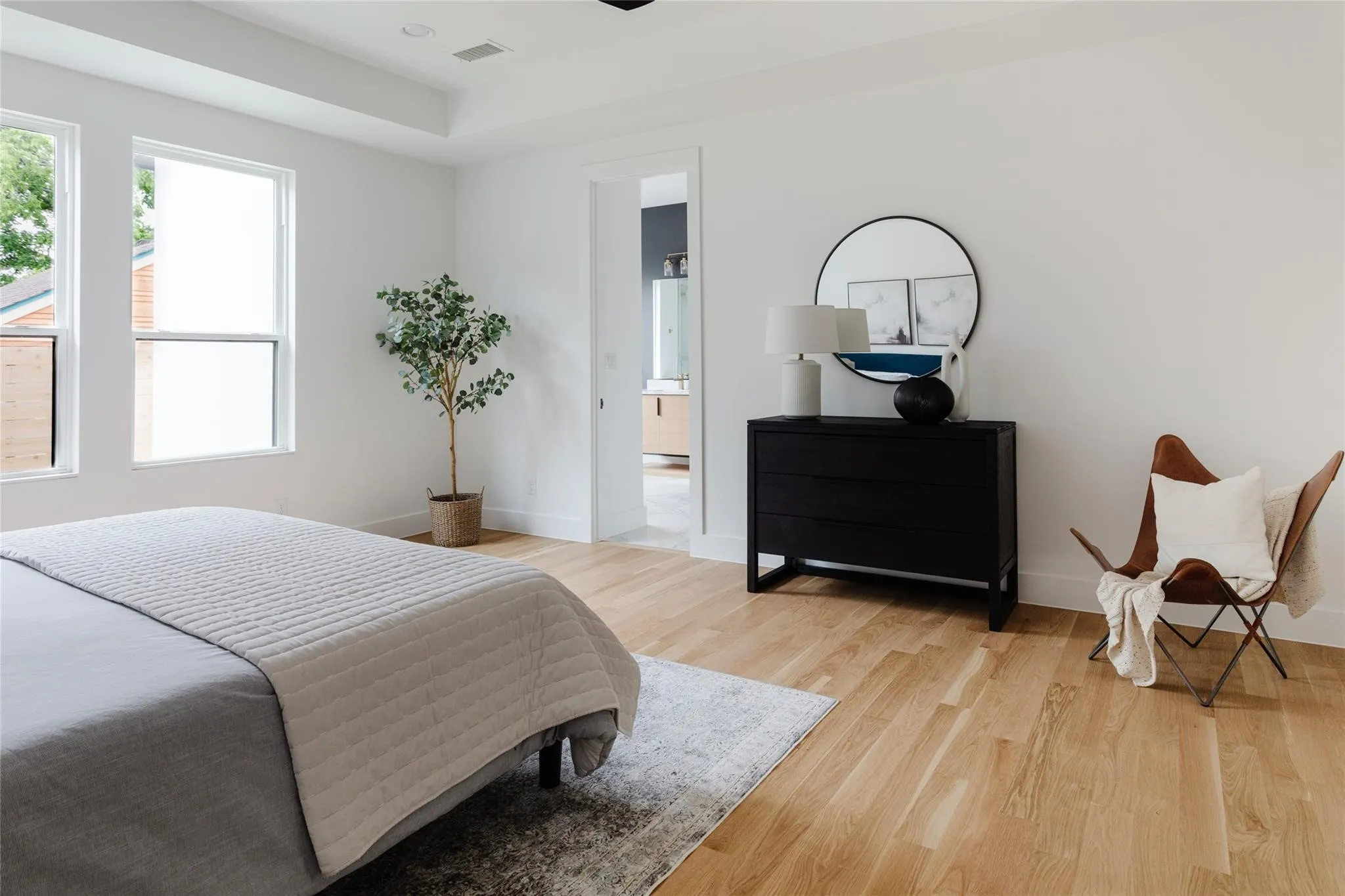Recessed ceiling lighting, light wood-finish flooring, two large windows, tray ceiling, and a doorway to an adjoining space