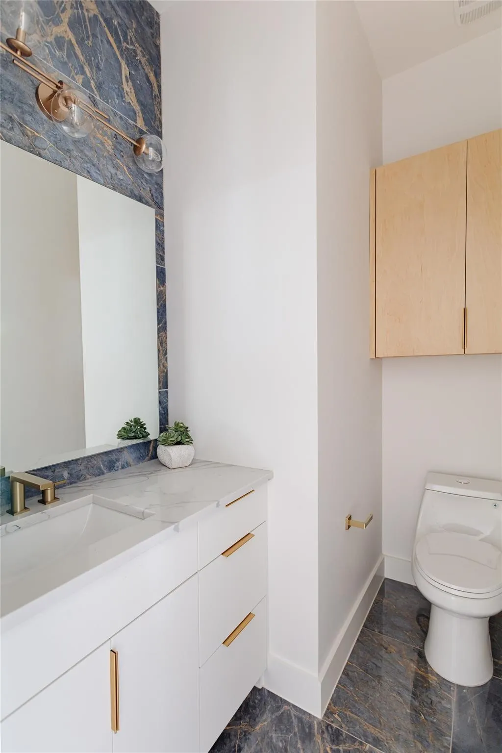 Built-in vanity with a single basin sink, gold-finish hardware, and a marble-pattern countertop