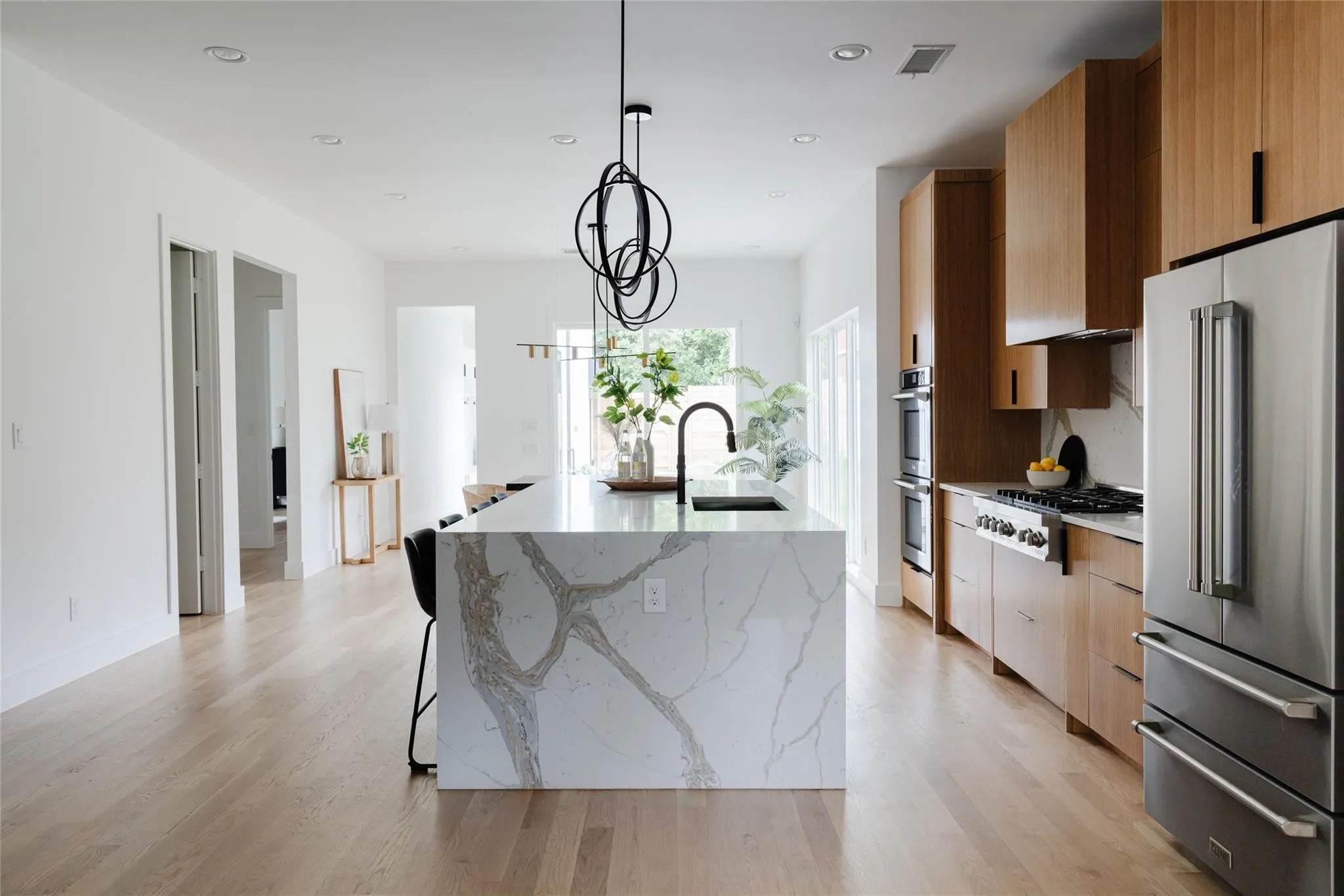 Gourmet kitchen with a waterfall island, integrated sink, stainless steel appliances, and custom wood cabinetry