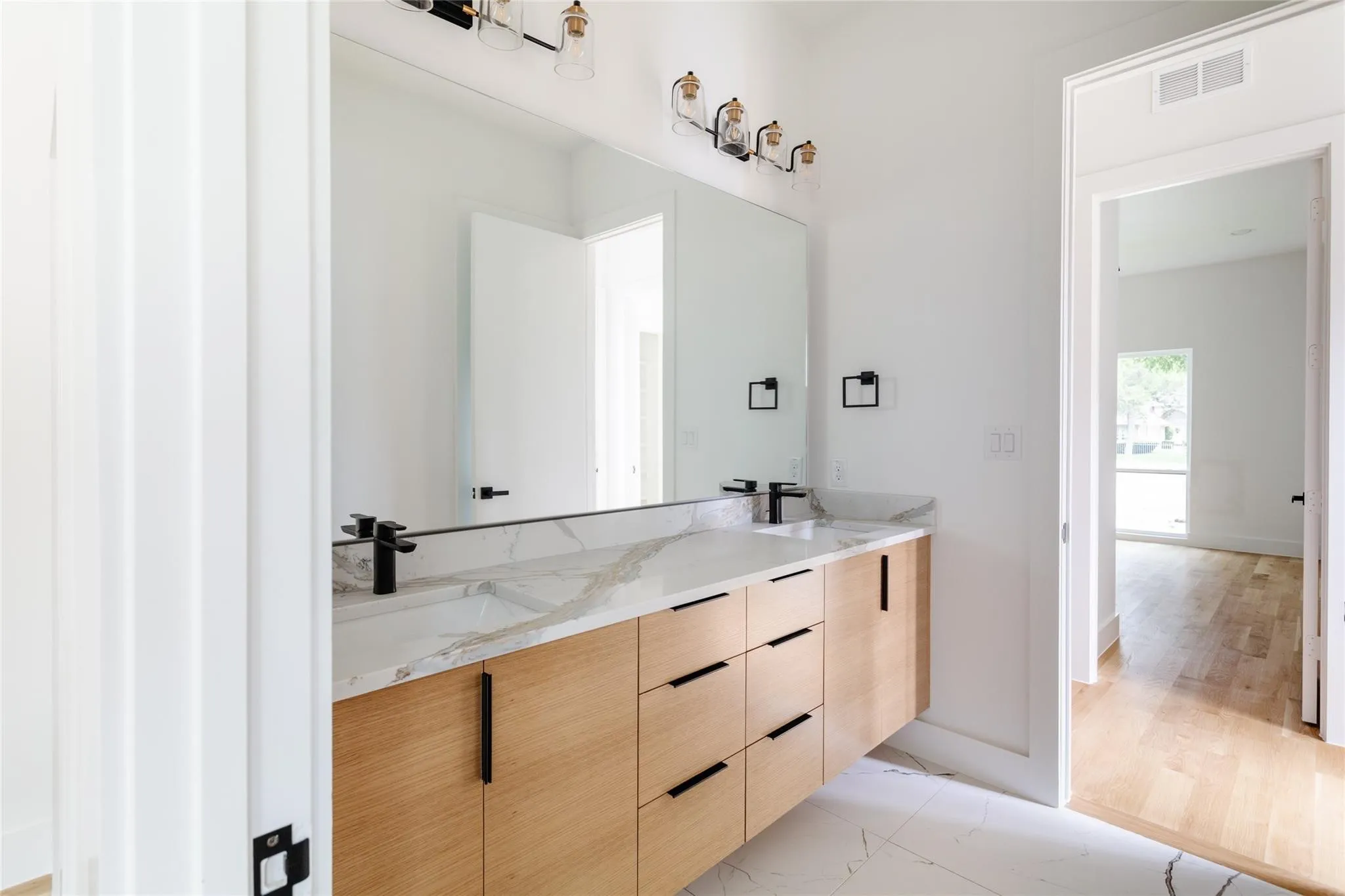 Dual vanity with wood-finish cabinetry, black hardware, and an integrated countertop with dual sinks