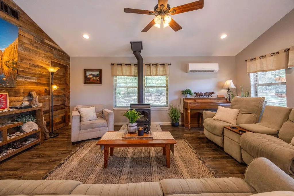 Vaulted ceiling, wood-finish flooring, accent wall with wood paneling, freestanding wood-burning stove, and ceiling fan with integrated lighting