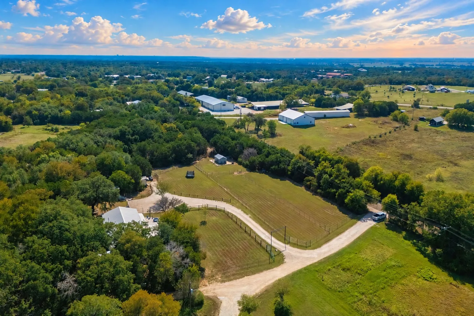 Expansive property featuring a white-roofed building, multiple outbuildings, and a gravel drive