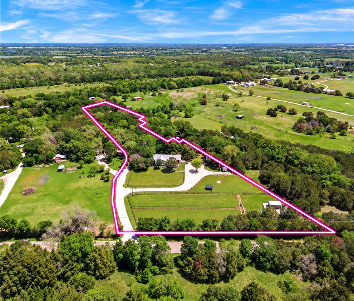 Expansive property featuring a main residence, additional structures, paved driveways, and surrounded by mature trees