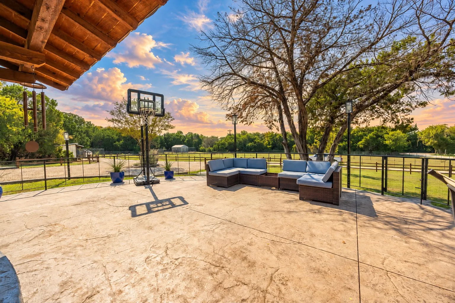 Expansive stamped concrete patio with an exposed wood beam overhang and black metal fencing