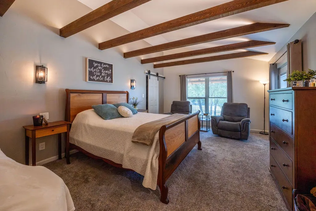 Vaulted ceiling with exposed wood beams, wall-mounted sconce lighting, window with exterior scenery, and barn door access