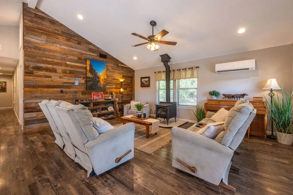 Vaulted ceiling with recessed lighting, wood-finish flooring, wood plank accent wall, wood-burning stove, and ceiling fan with light fixture