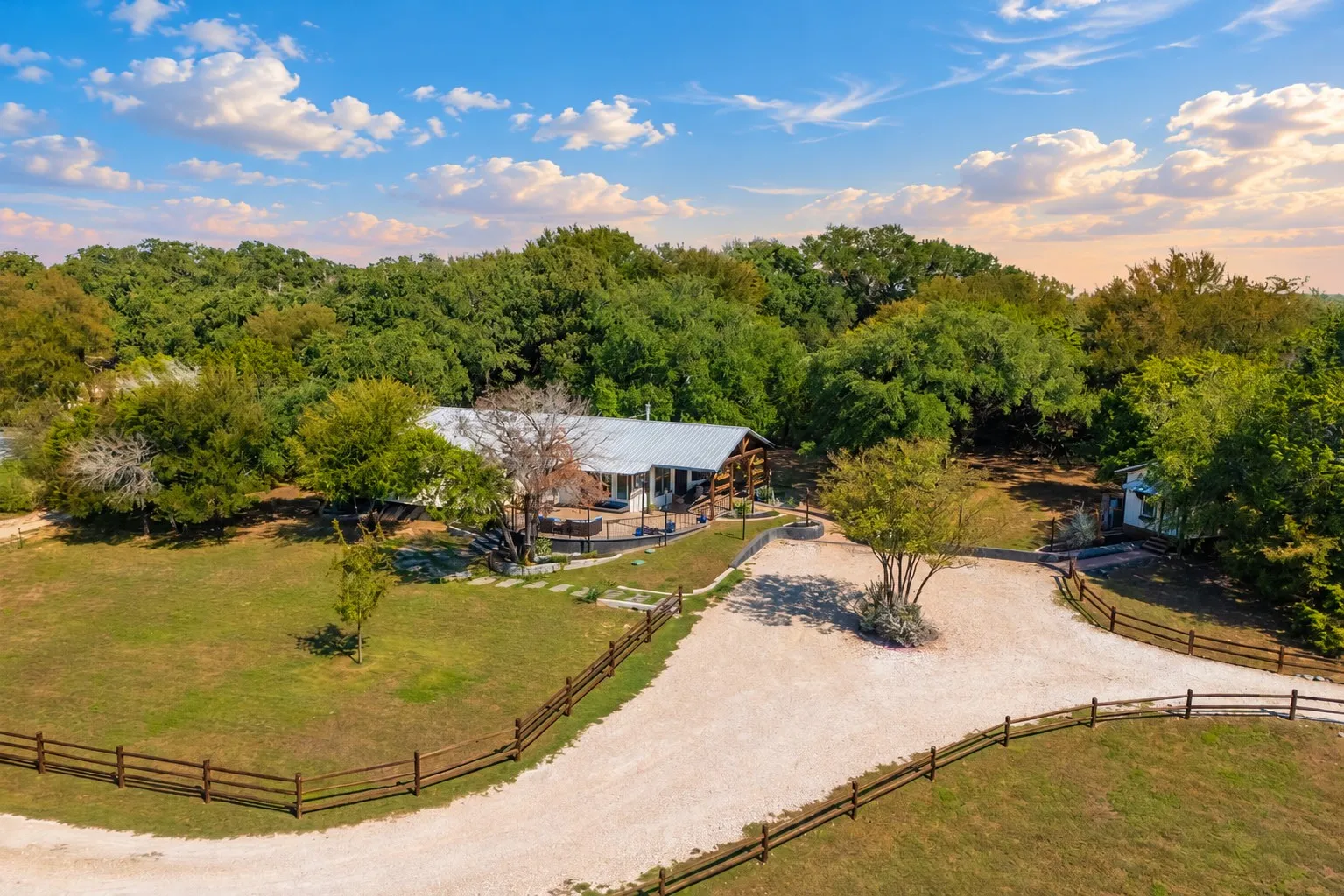 Expansive property featuring a gravel driveway, wood fencing, a single-story residence with a metal roof, and abundant mature trees