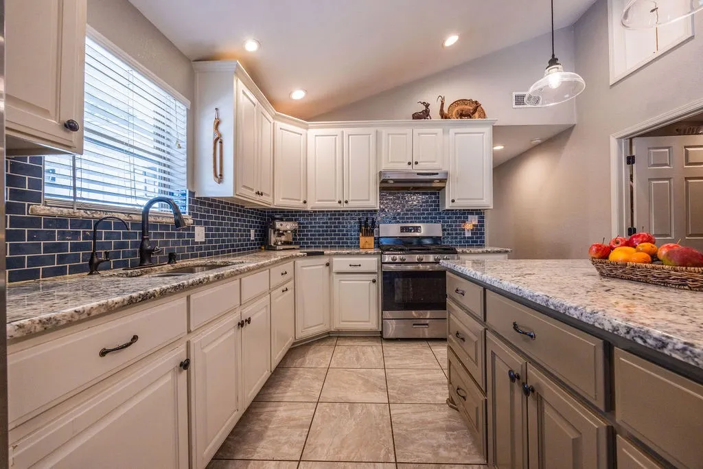Kitchen featuring white cabinetry, subway tile backsplash, stainless steel appliances, granite countertops, and tile flooring