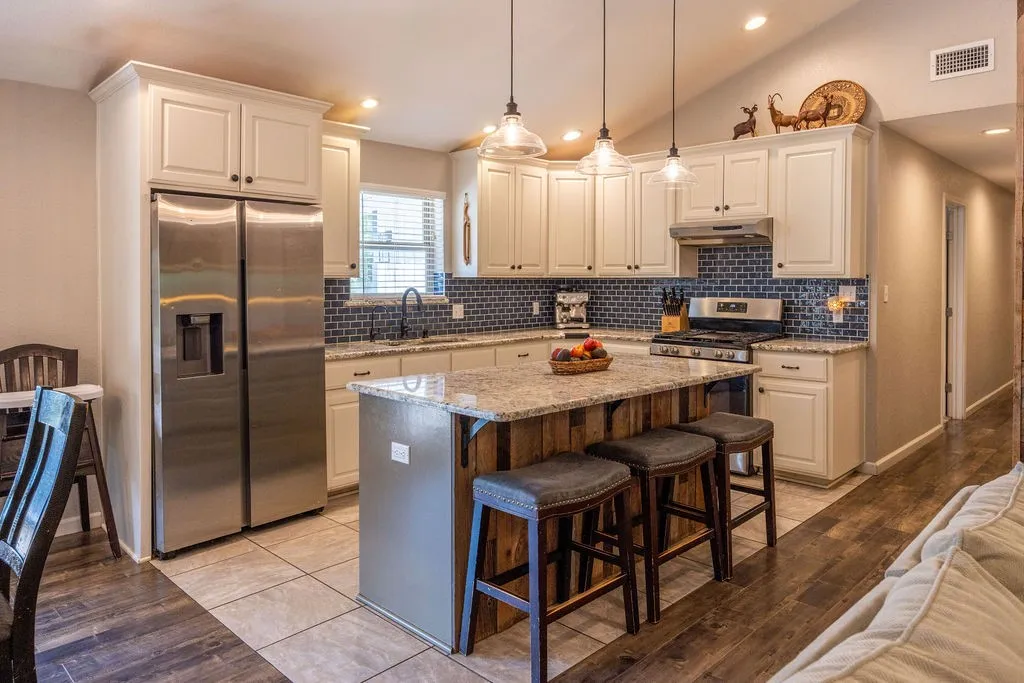 Kitchen featuring white cabinetry, a large kitchen island with counter seating, stainless steel appliances, a dark tile backsplash, and recessed lighting