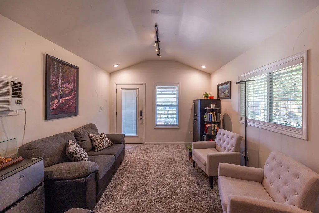Vaulted ceiling, track lighting, neutral wall finishes, window with blinds, and paneled door
