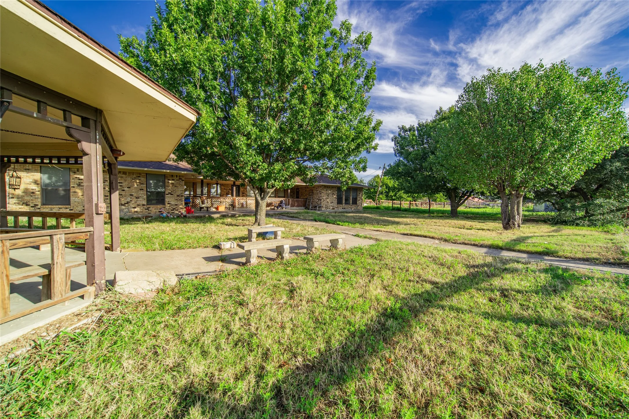 Expansive outdoor area featuring mature trees, a paved walkway, and a covered porch