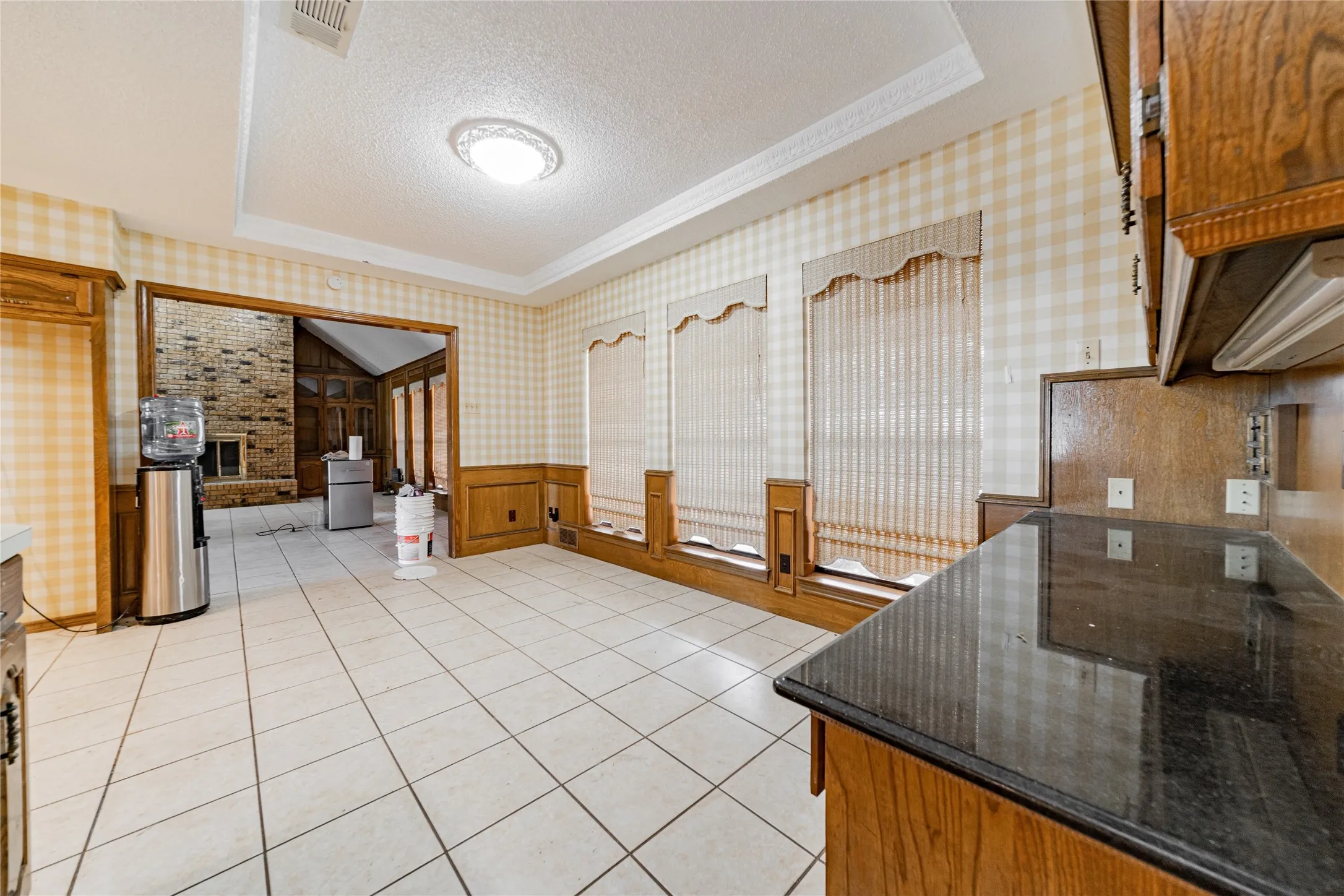 Tile flooring, dark countertops, wood cabinetry, wainscoting, and recessed ceiling with decorative molding