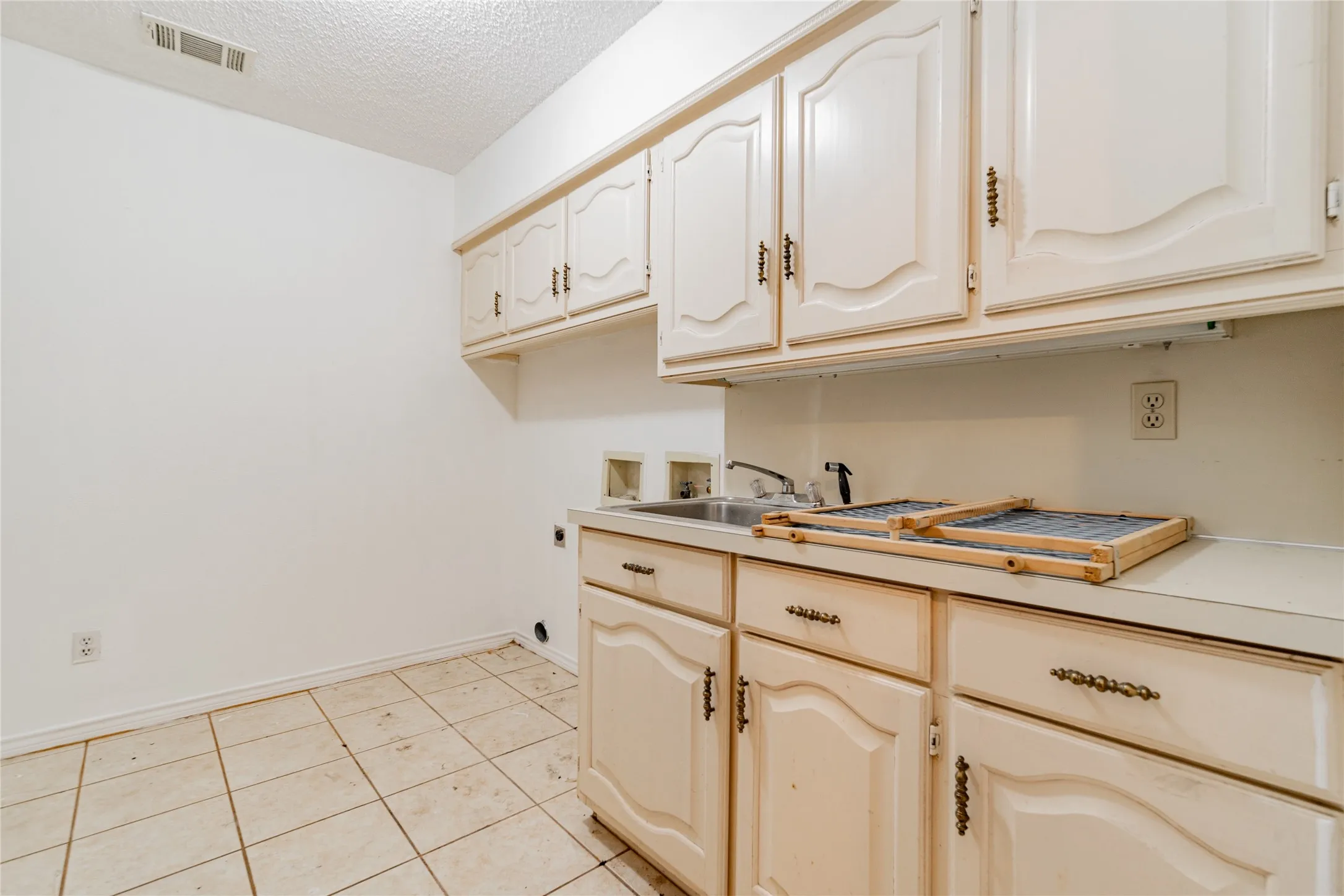 Functional laundry area featuring upper and lower cabinetry, a utility sink, and tile flooring