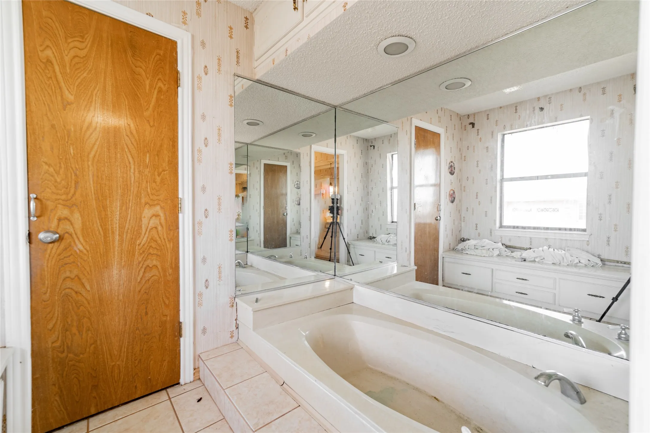 Built-in bathtub with tiled surround, mirrored wall, window with storage bench, and recessed lighting