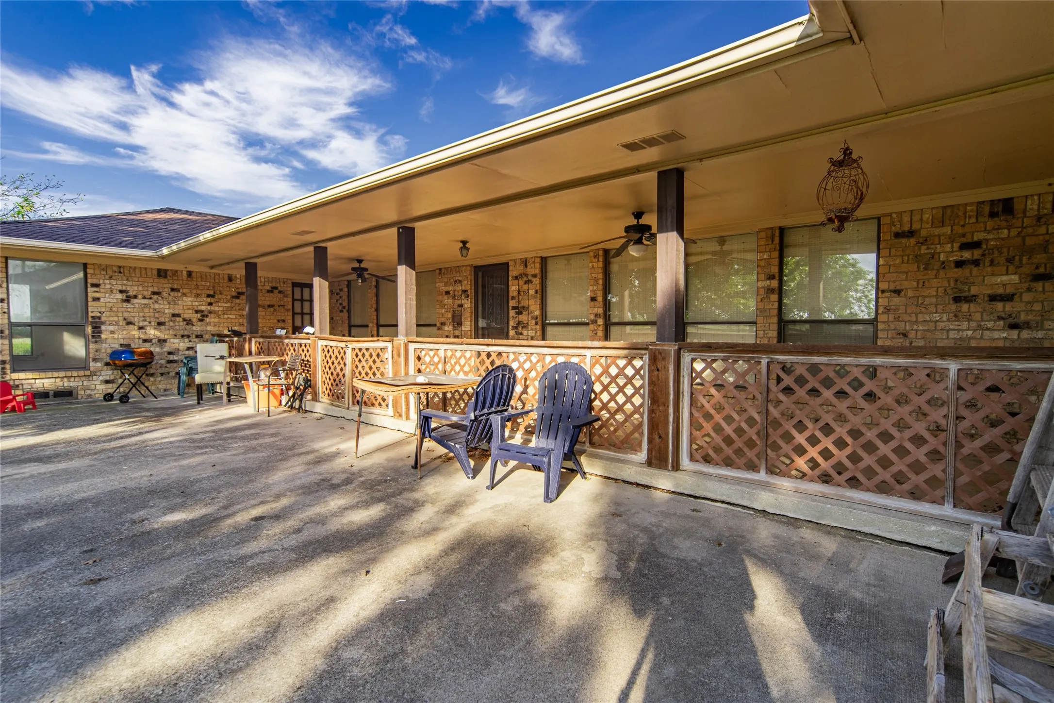 Expansive concrete patio with a covered porch featuring ceiling fans, lattice detailing, and exterior lighting