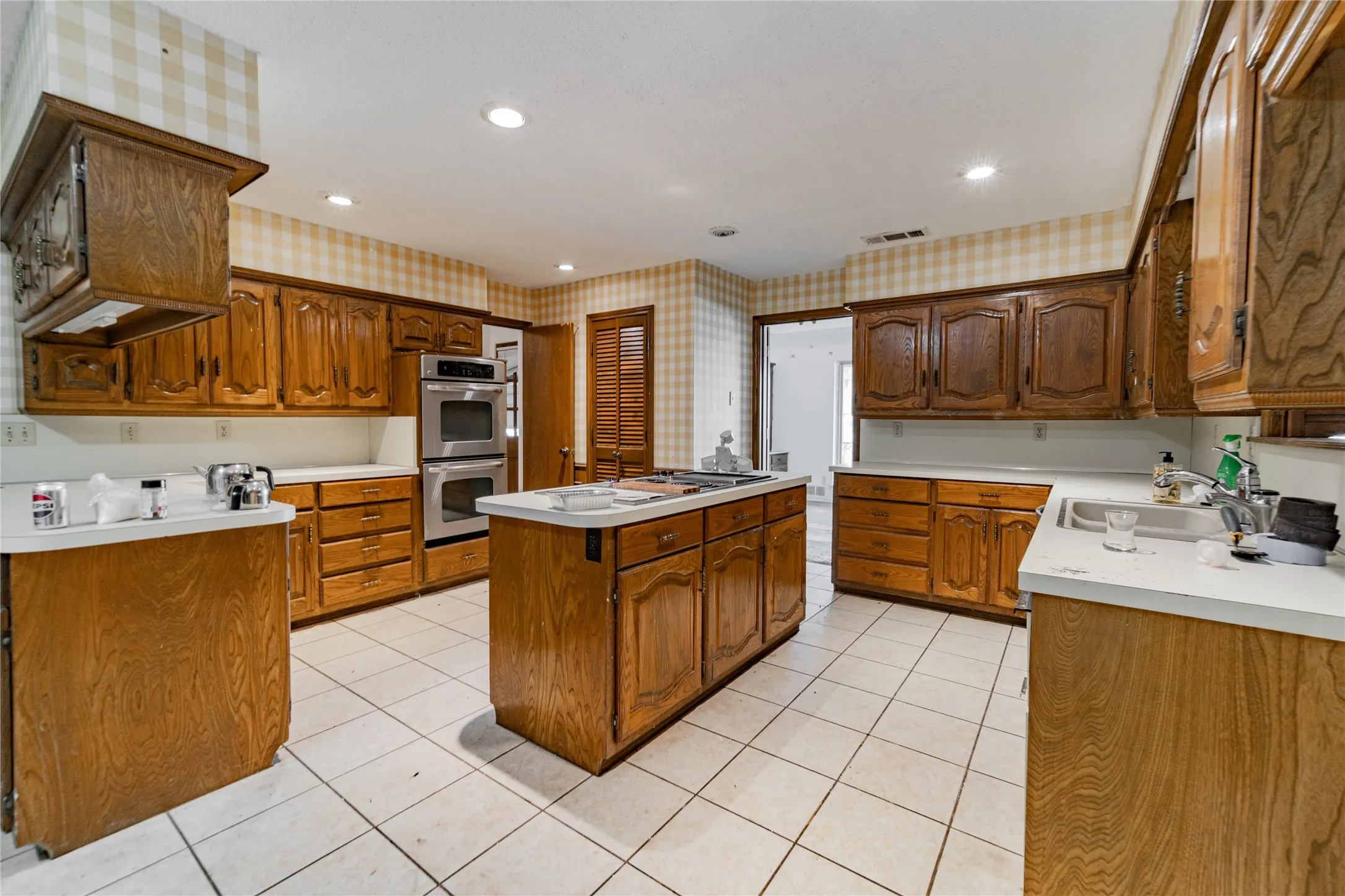 Kitchen featuring a central island, extensive wood cabinetry, white countertops, stainless steel double ovens, and tile flooring