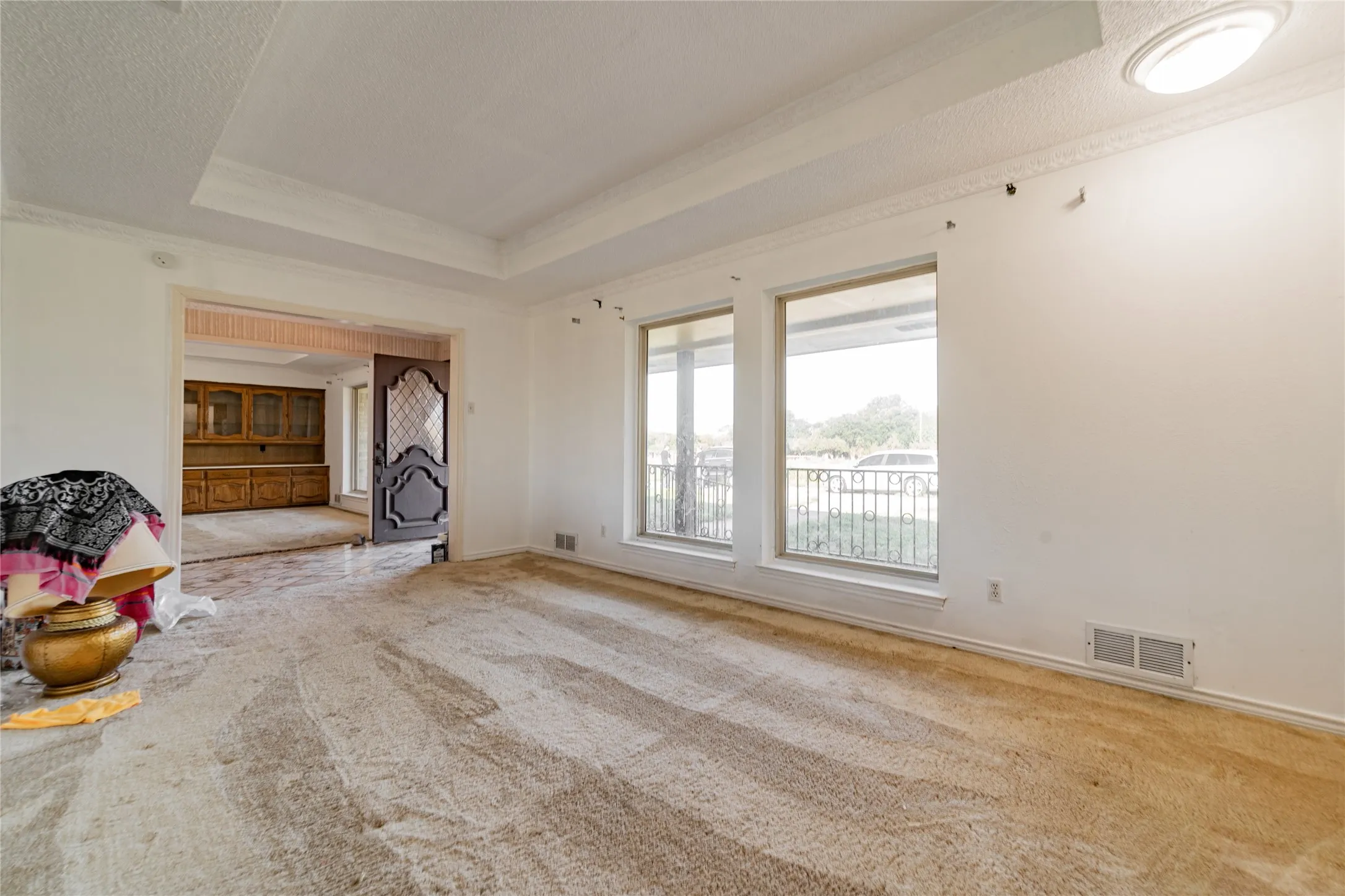 Tray ceiling with crown molding, dual large windows, and an arched doorway leading to an additional space featuring built-in cabinetry