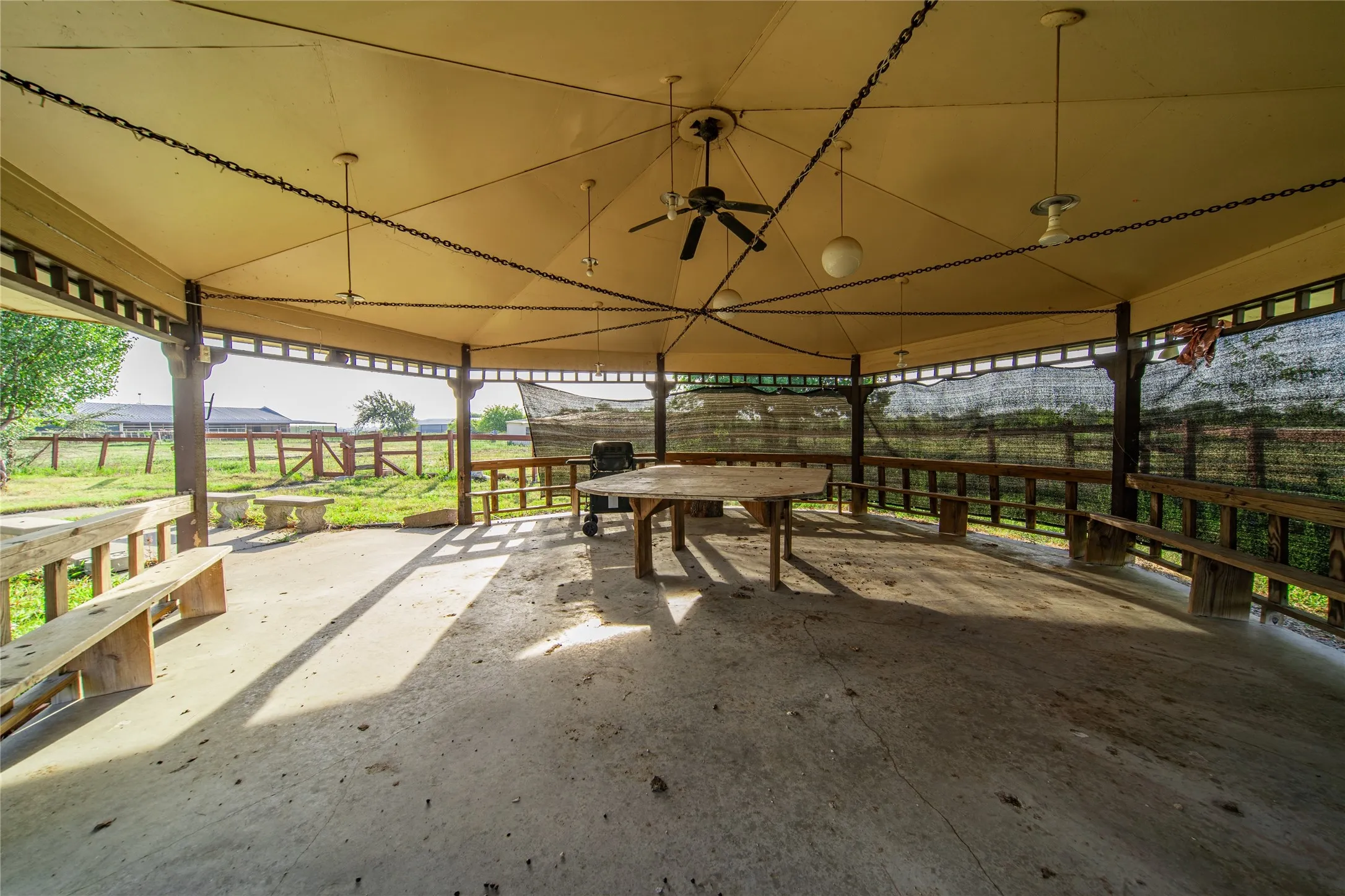 Expansive outdoor pavilion with a concrete floor, equipped with ceiling fans and mounted lighting fixtures