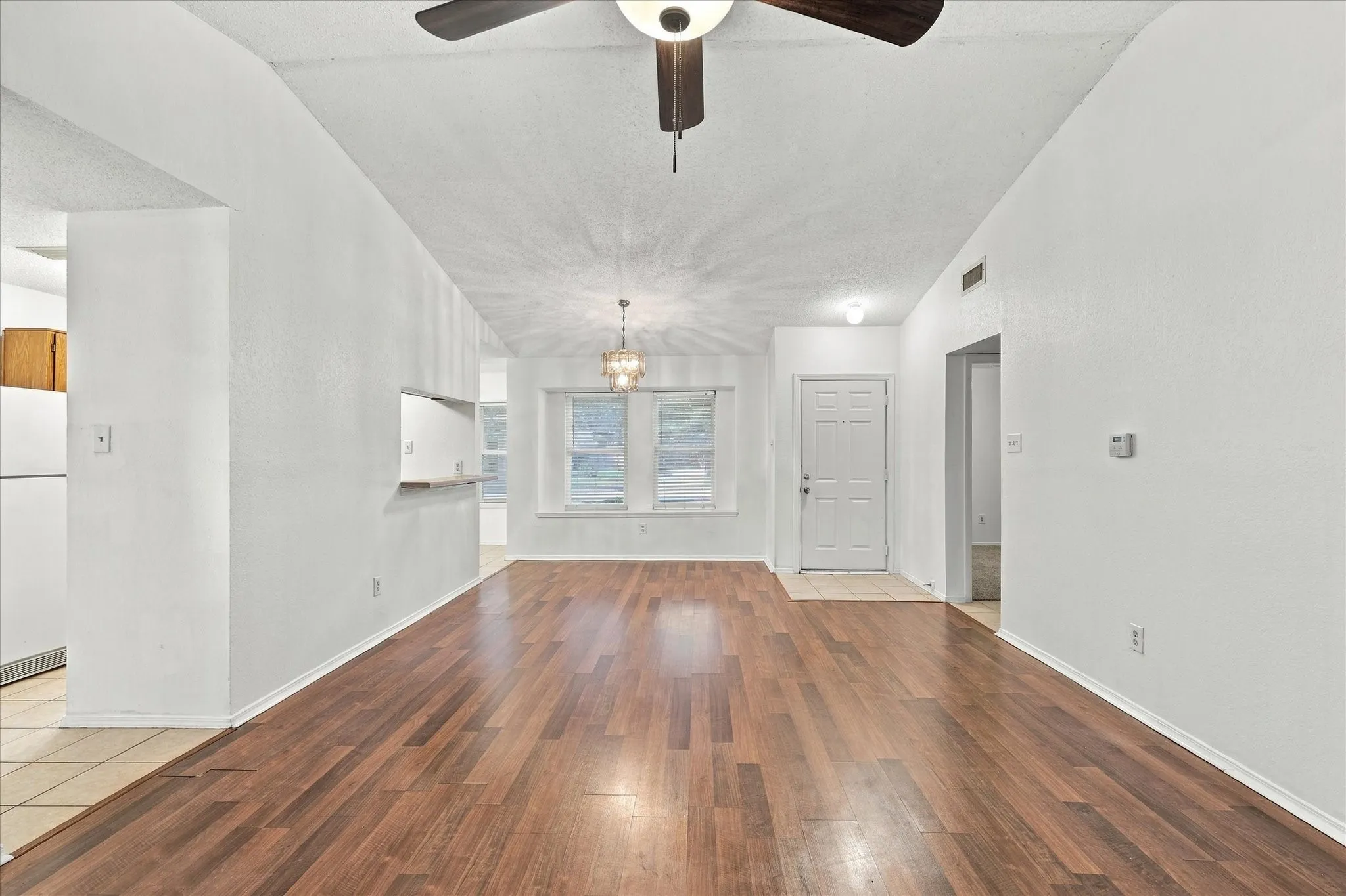 Vaulted ceilings, wood-finish flooring, two windows, and a pass-through opening to the kitchen