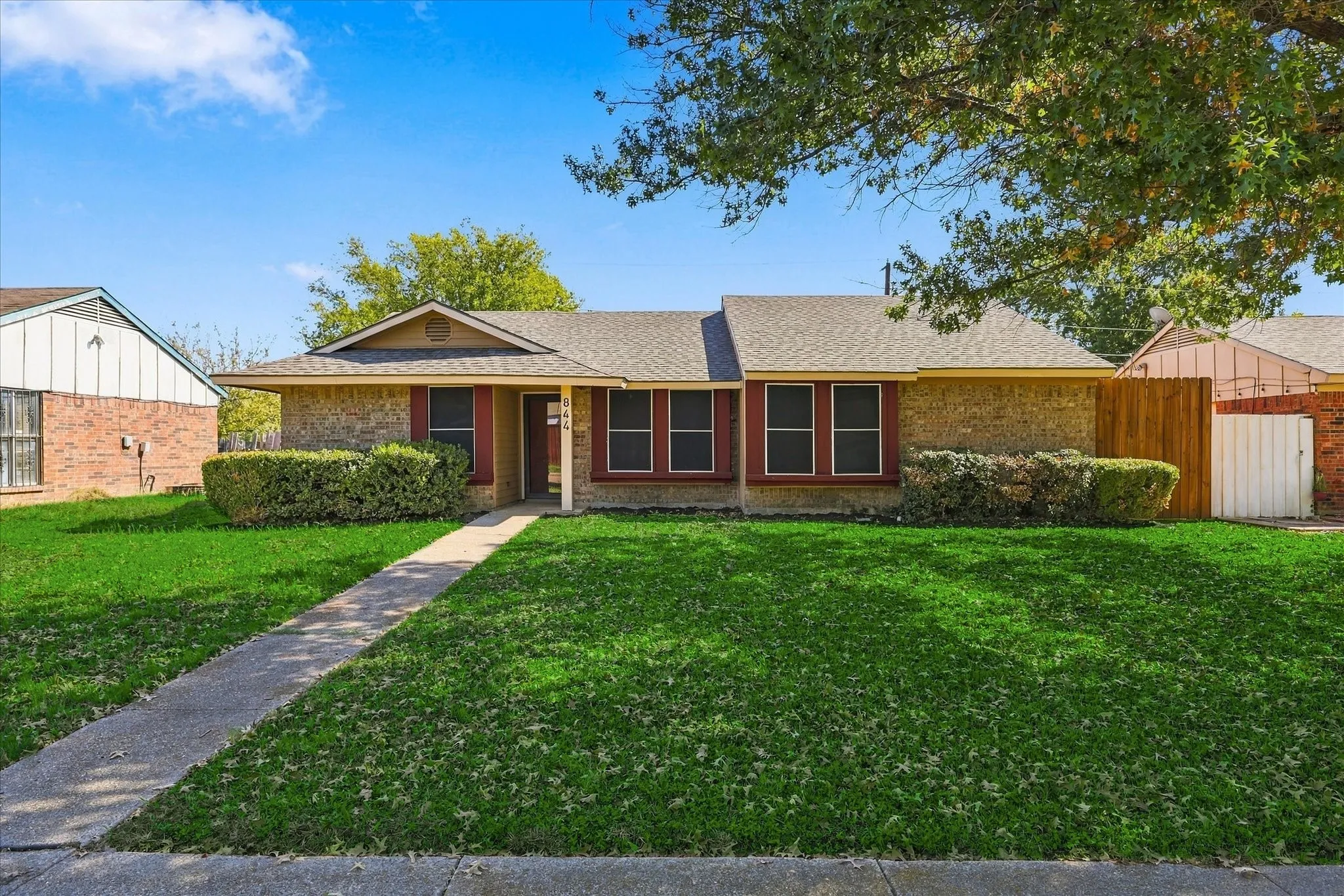 Brick facade, gabled entry, red window shutters, concrete walkway, and a wooden fence
