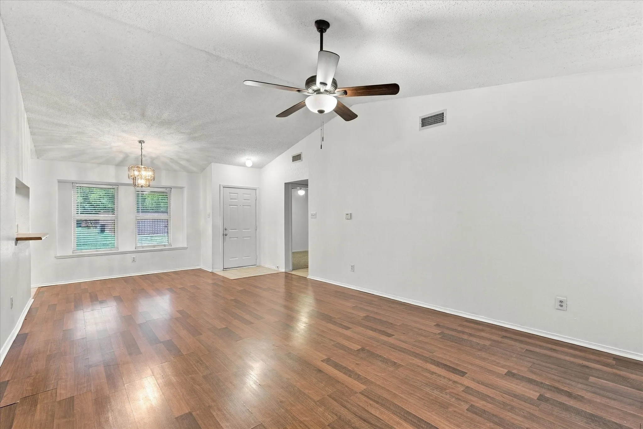 Vaulted ceiling with a ceiling fan, recessed lighting, wood-finish flooring, white walls, and a decorative chandelier