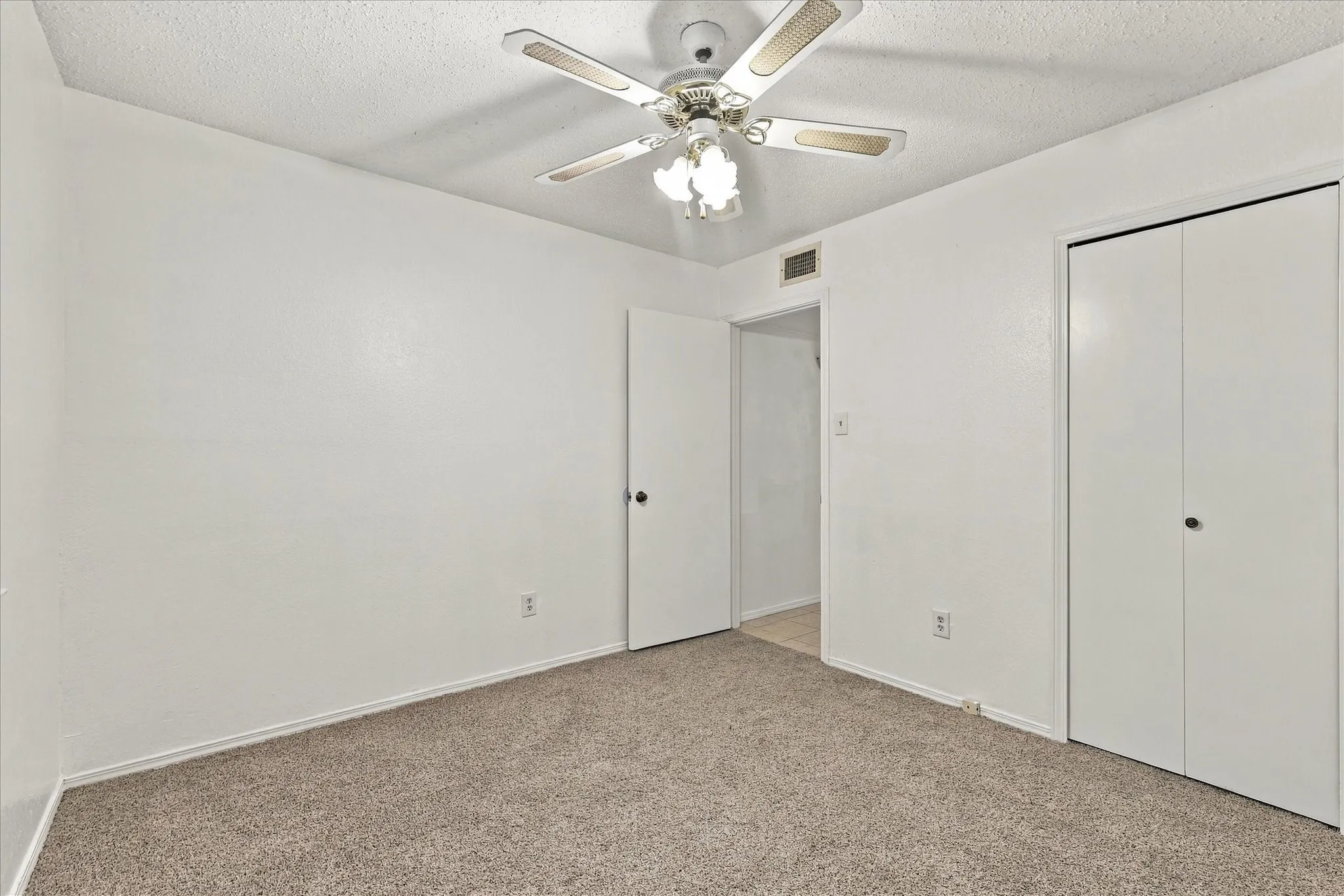 Neutral wall finishes, textured ceiling, ceiling fan with integrated lighting, and carpeted flooring