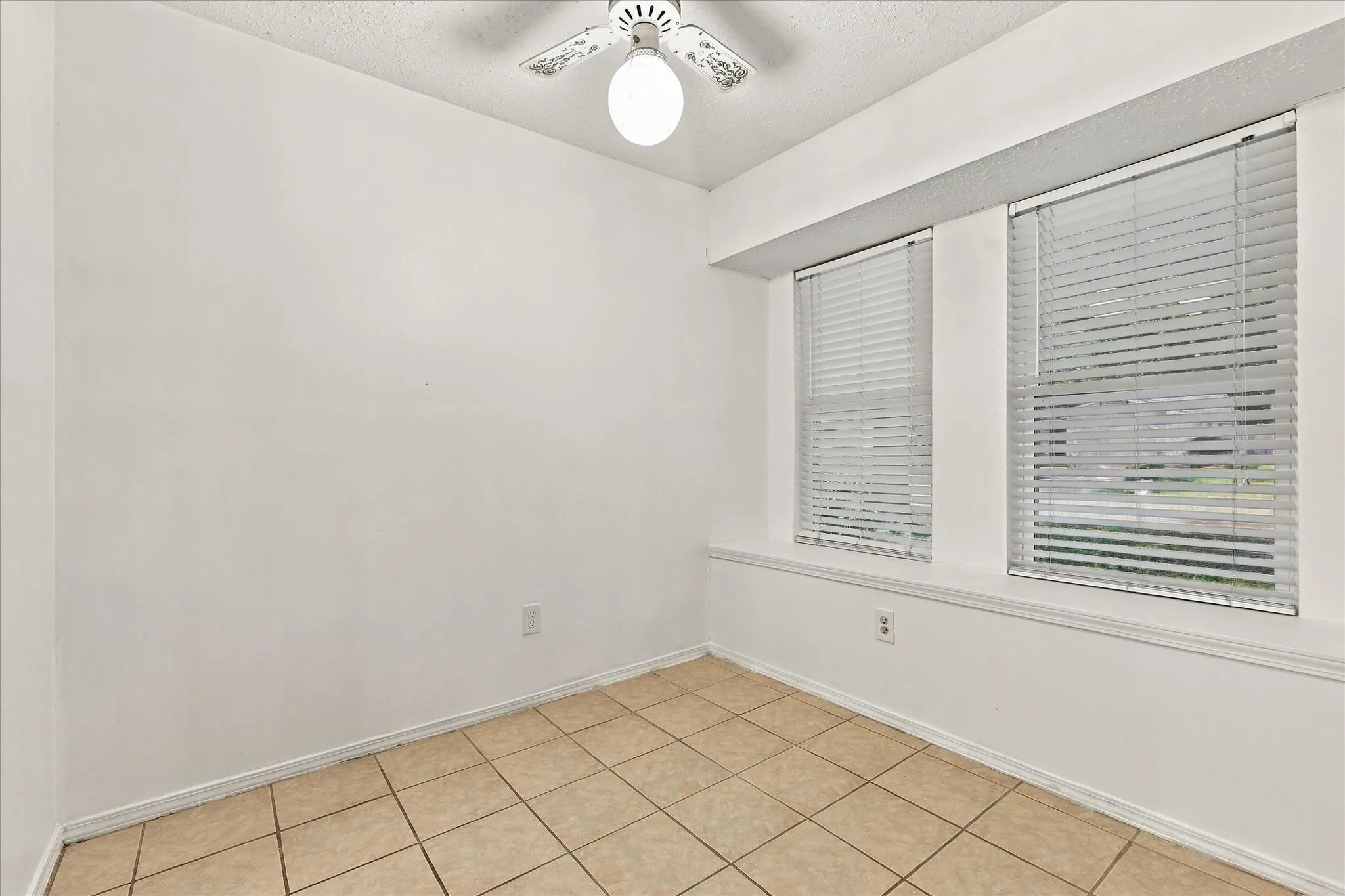 White walls with a textured ceiling, tile flooring, and a ceiling fan with integrated lighting