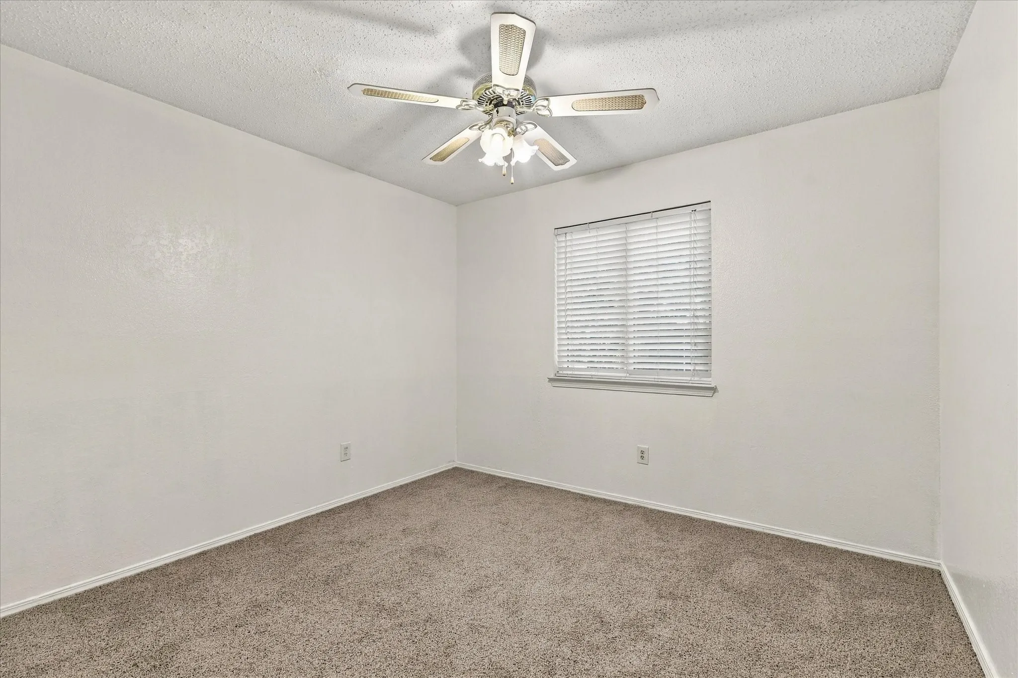 Neutral carpeted flooring, white painted walls, a window with horizontal blinds, and a ceiling fan with integrated lighting