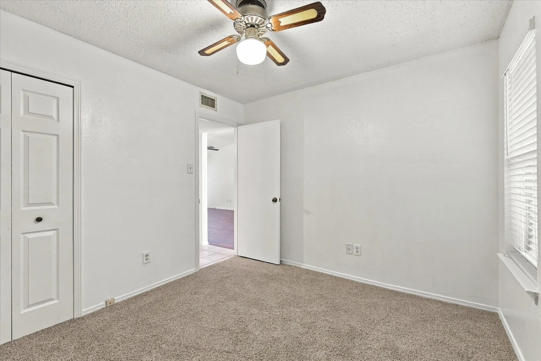 Neutral-toned carpeting, ceiling fan with light fixture, and window with blinds