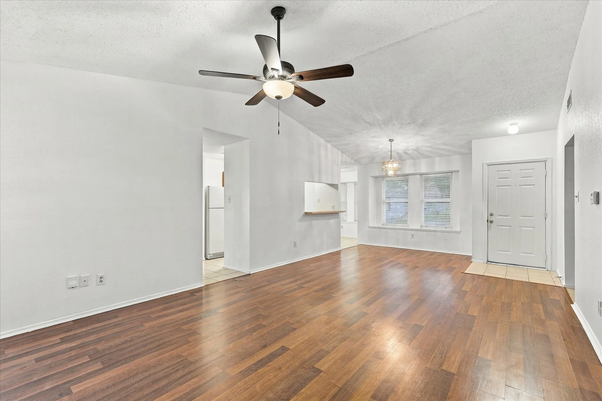 Wood-finish flooring throughout, vaulted ceiling, built-in ceiling fan, white paneled entry door, and multiple windows with white trim