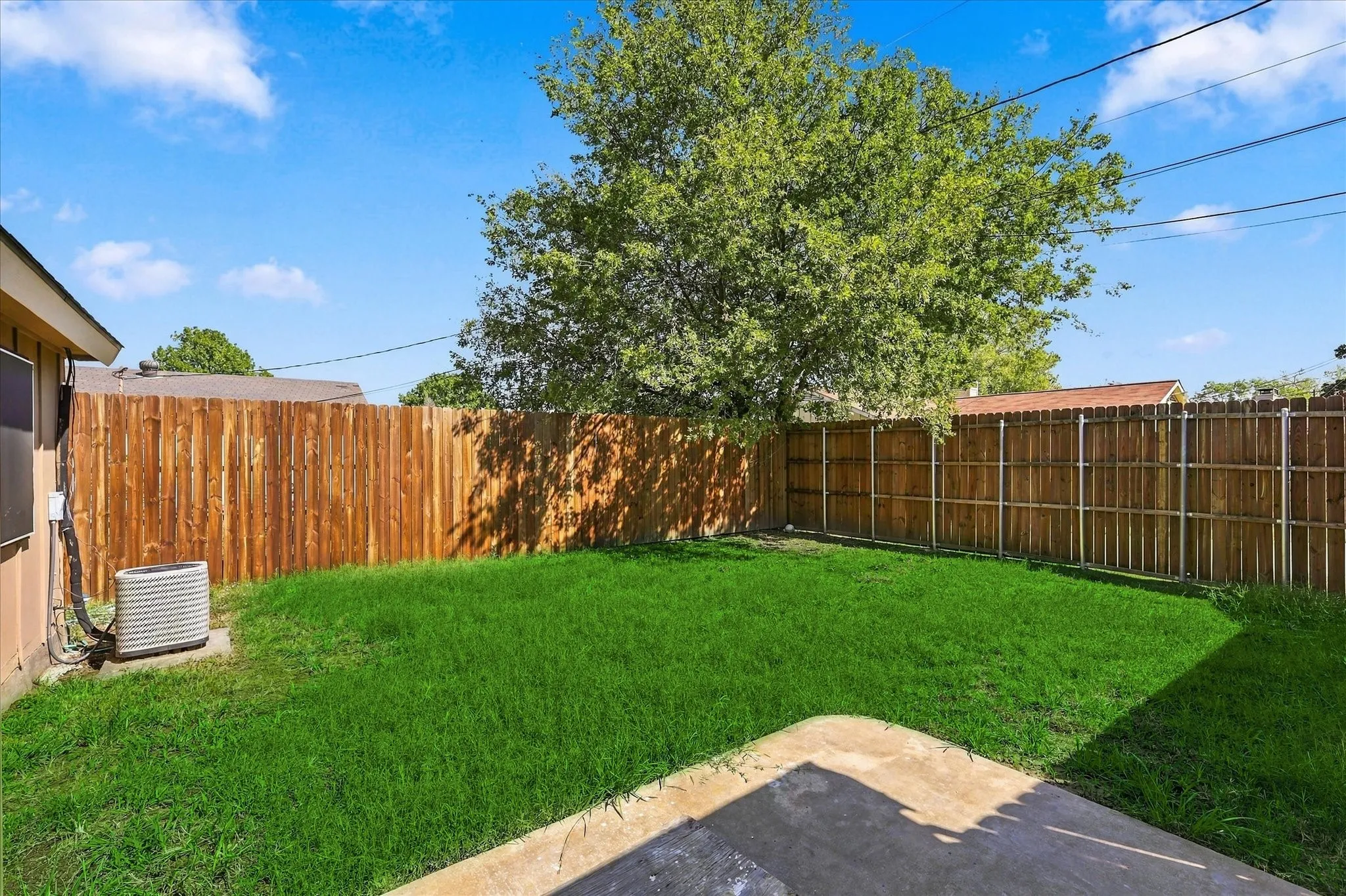 Expansive backyard featuring a manicured lawn, full privacy fencing, and mature tree