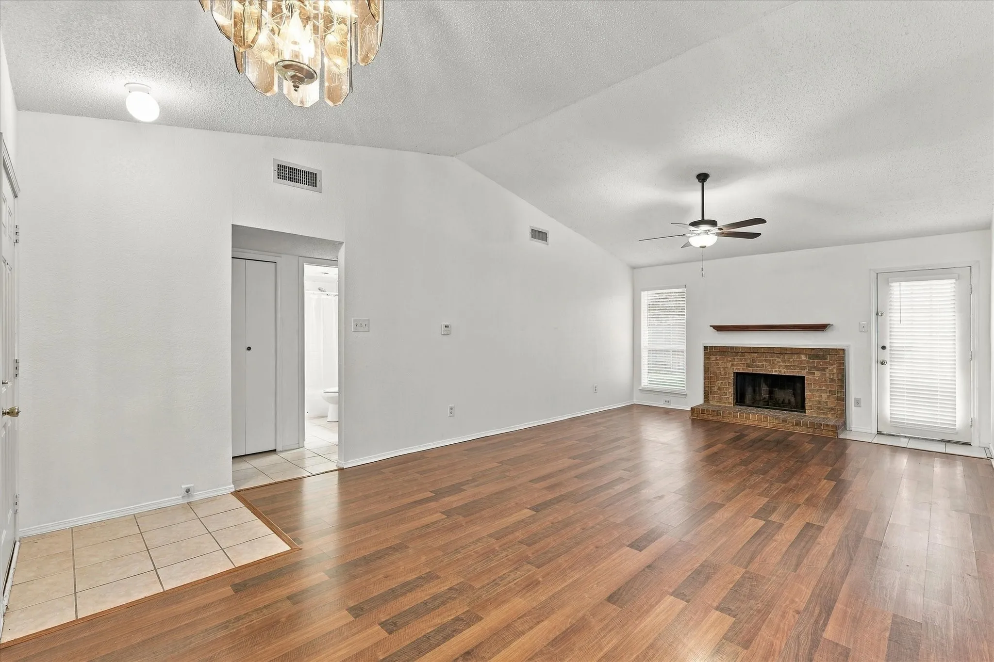 Vaulted ceiling with a ceiling fan, wood-finish flooring, brick-surround fireplace with a wood mantel, and an exterior door