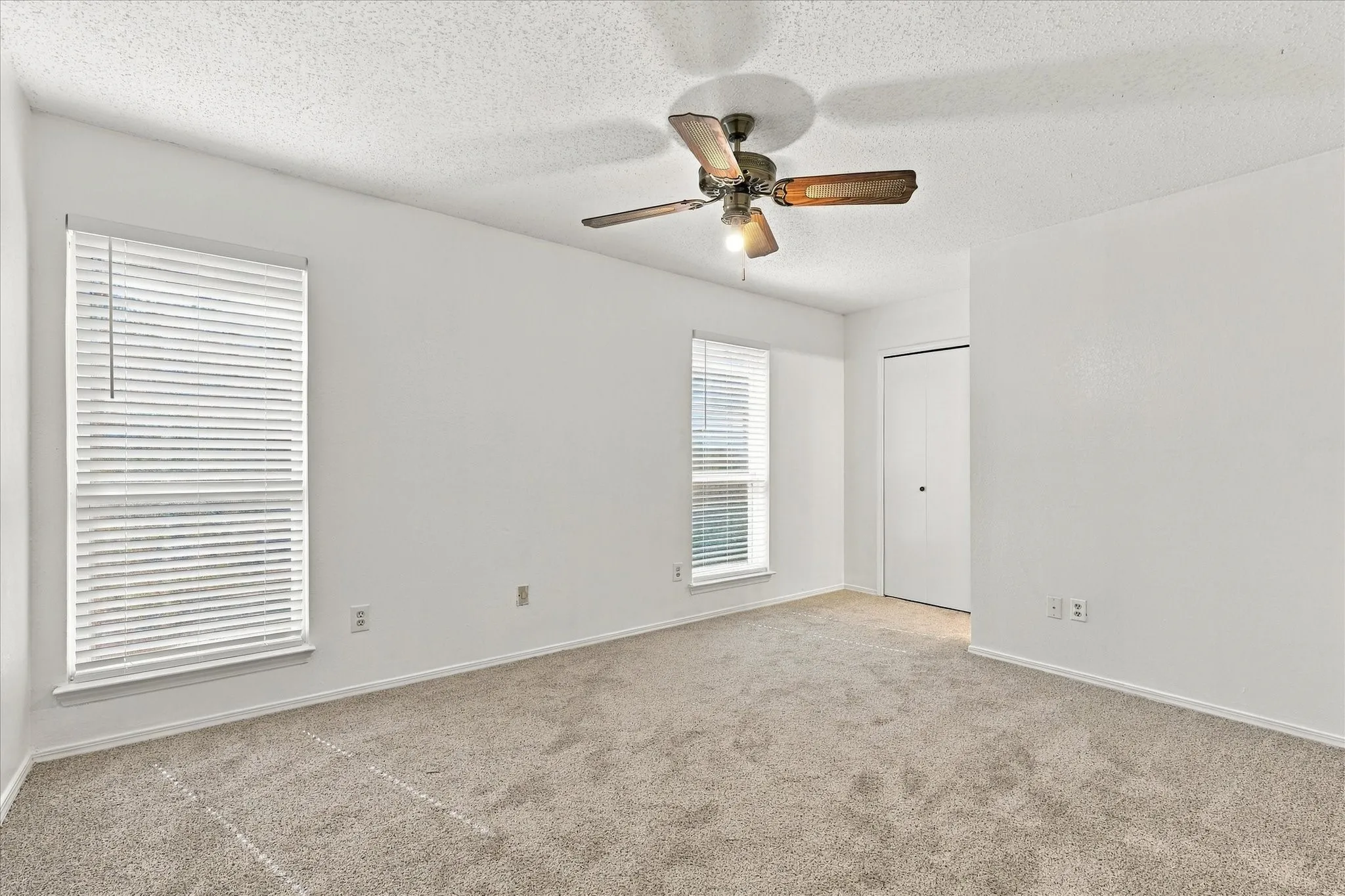 Carpeted room featuring two windows with horizontal blinds, a ceiling fan with light fixture, and a built-in closet with bifold doors