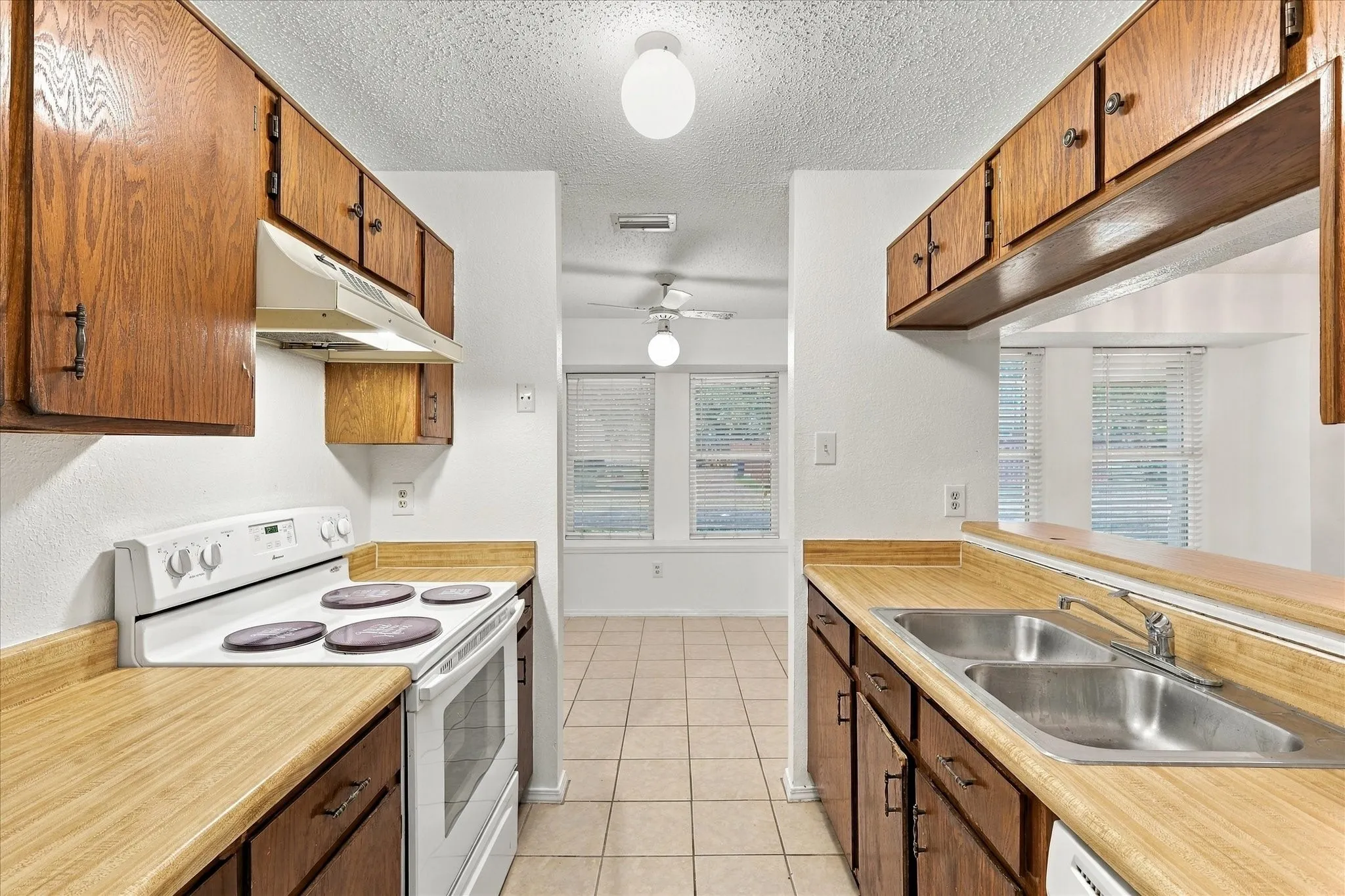 Galley kitchen featuring wood-finish cabinetry, a double basin stainless steel sink, a built-in range, and tile flooring