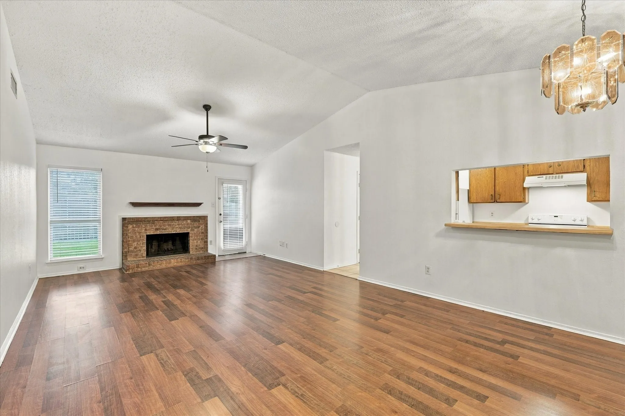 Vaulted ceiling with wood-finish flooring, brick fireplace with mantel, and a built-in kitchen pass-through