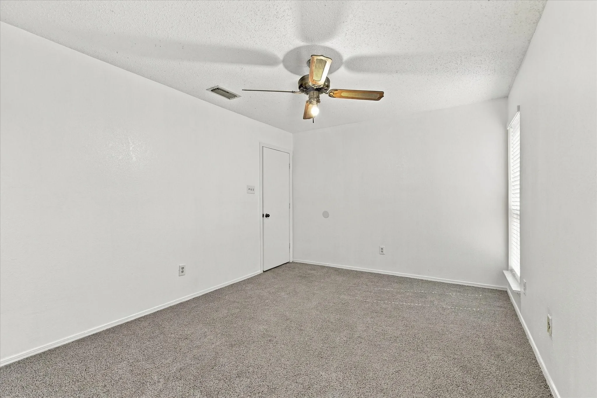 Neutral white walls with textured finish, carpeted flooring, window with blinds, and a ceiling fan with integrated lighting