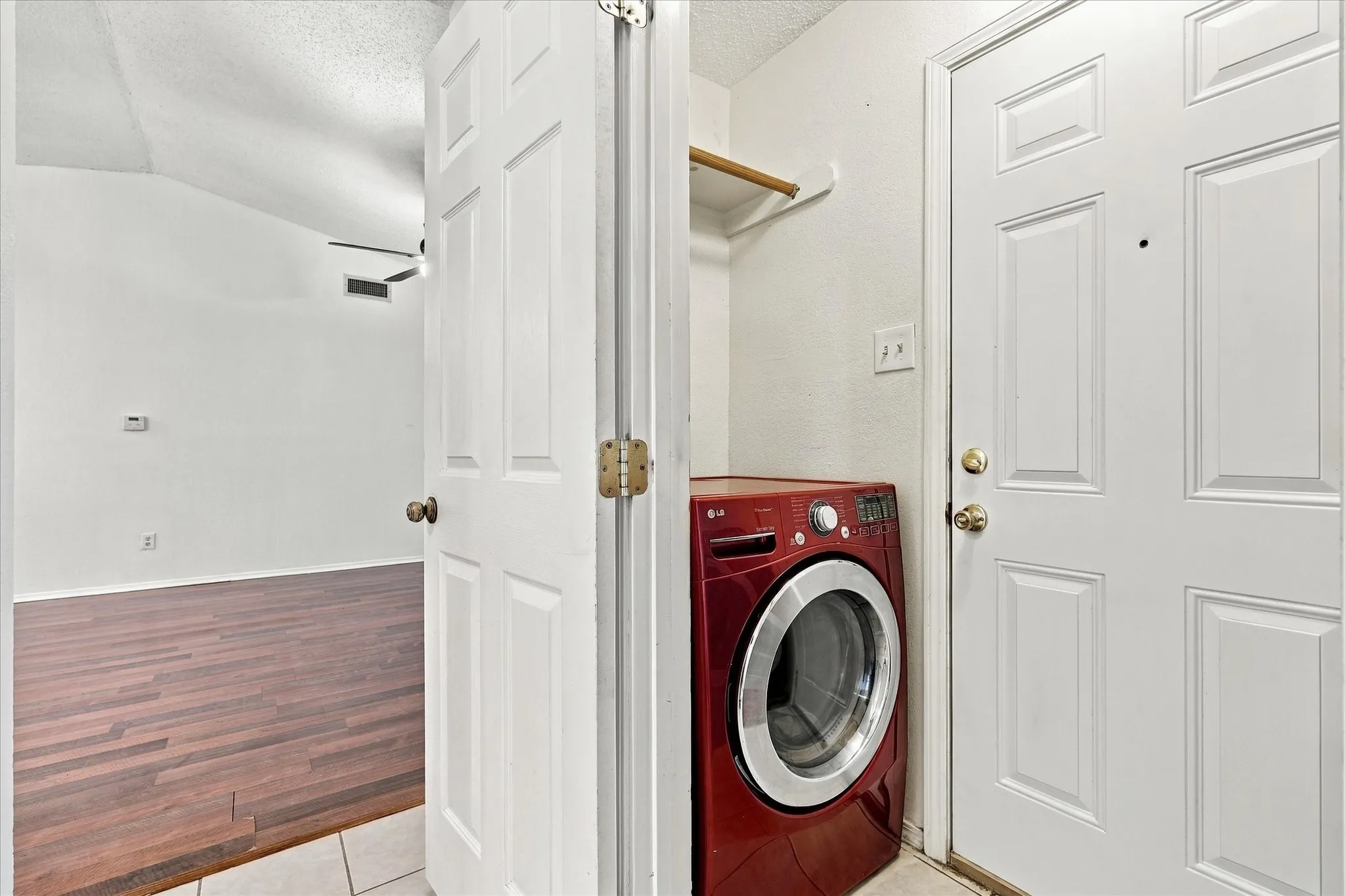 Dedicated laundry area with a built-in shelf, adjacent to a room with wood-finish flooring and a vaulted ceiling