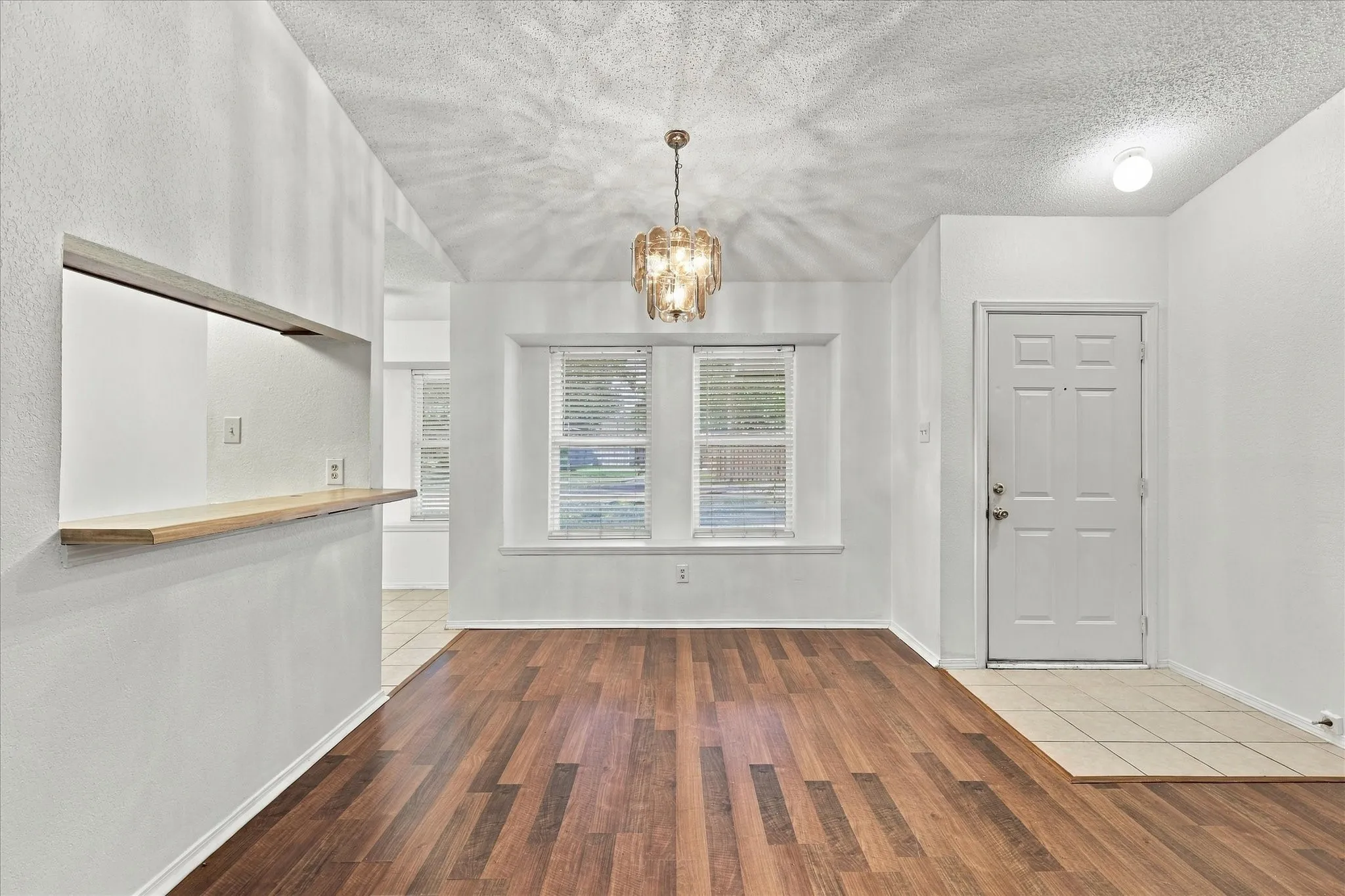 Vaulted ceiling, wood-finish flooring, pass-through window with wood counter, decorative chandelier, and paneled entry door with tile flooring