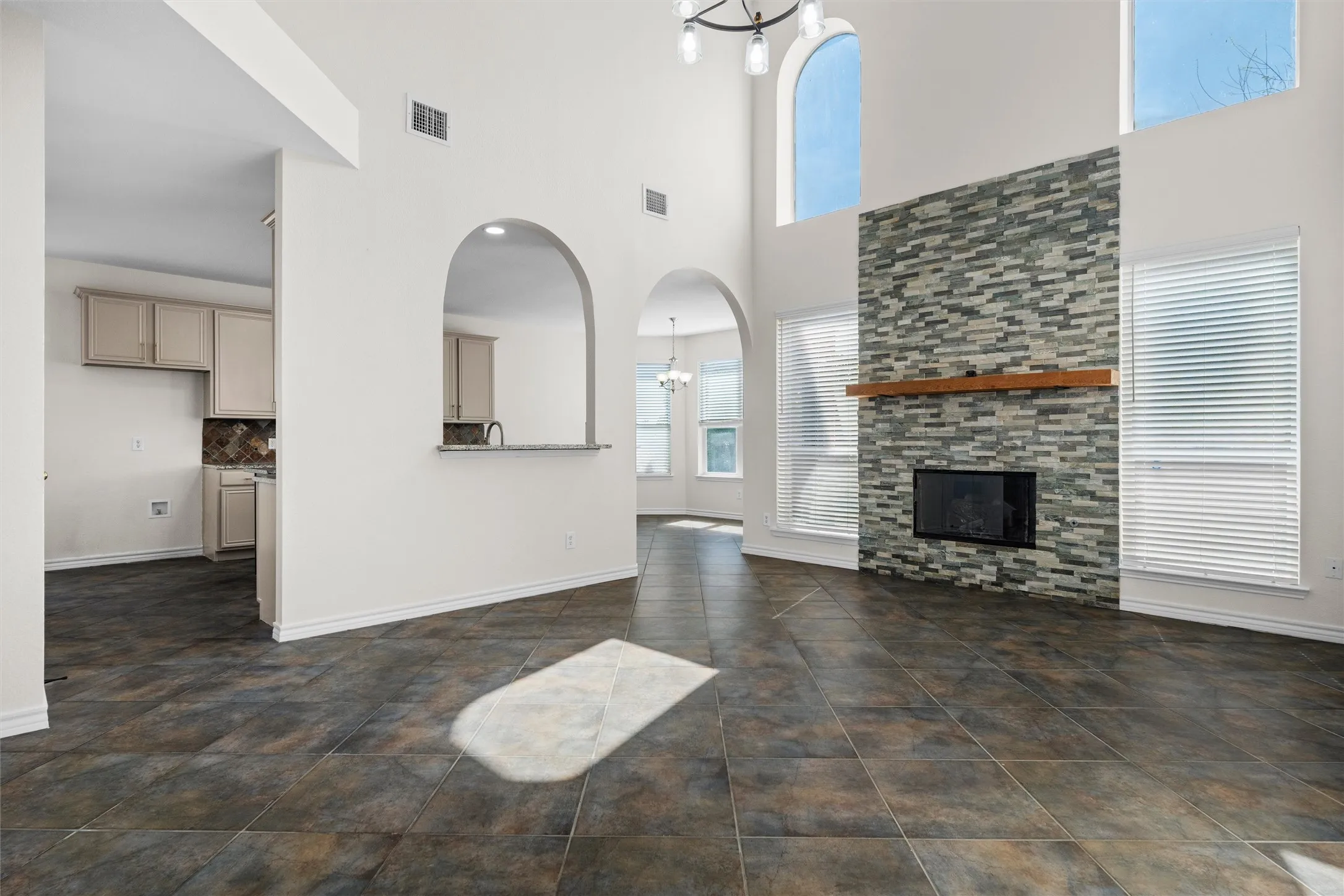 Vaulted ceilings with an arched window, a stone-clad fireplace with a wood mantel, tiled flooring, and arched doorways